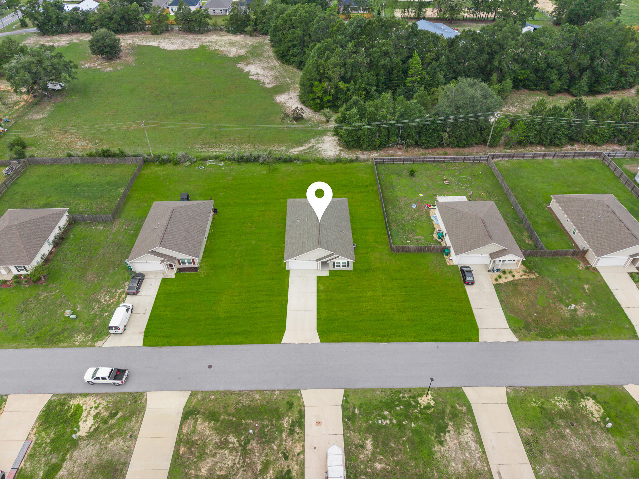 Aerial view of a single-story home with a broad lawn and neighboring wooded land.