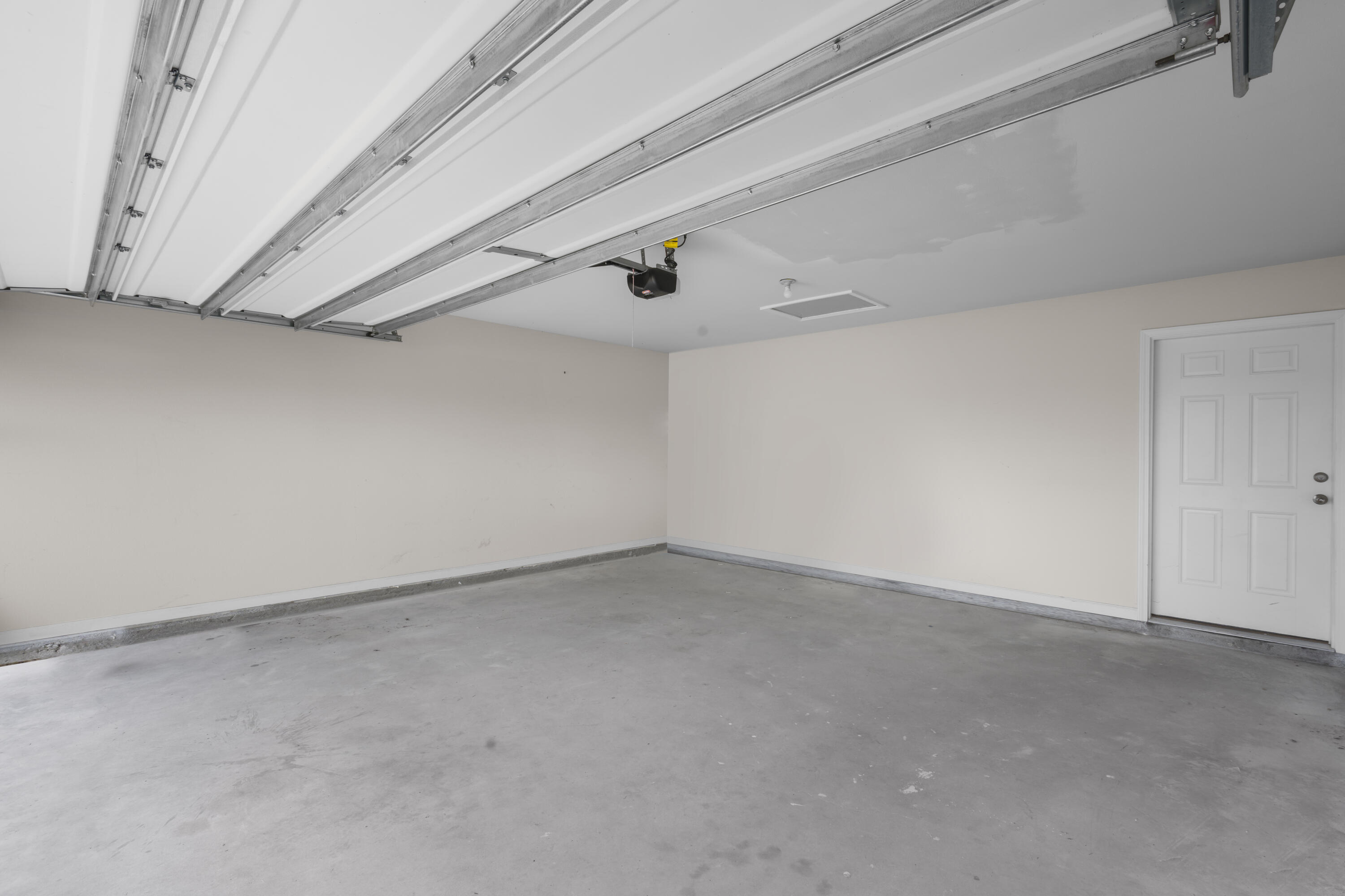 Empty garage with a raised overhead door, concrete floor, and white interior door.
