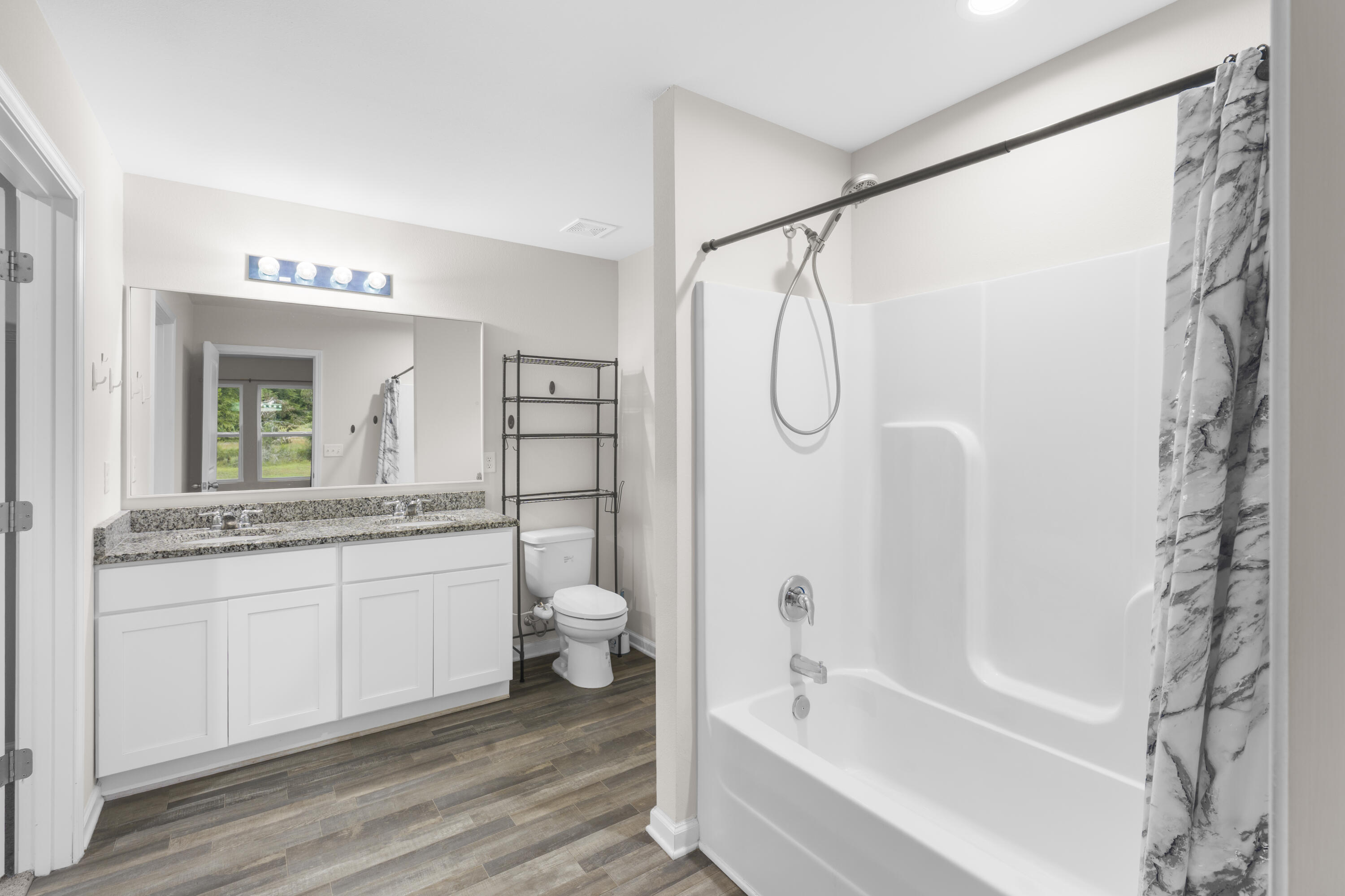 Bathroom with a white tub and shower, granite vanity, large mirror, and wood-look tile floor.