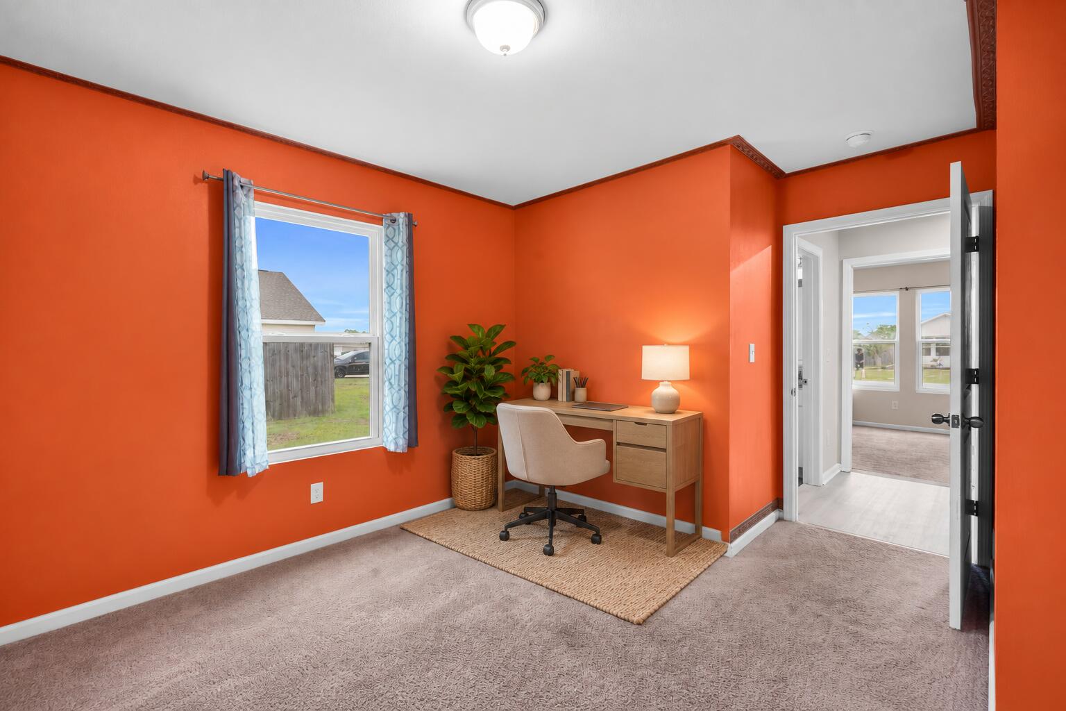 Furnished home office with bright orange walls, a desk by the window, and an open doorway.