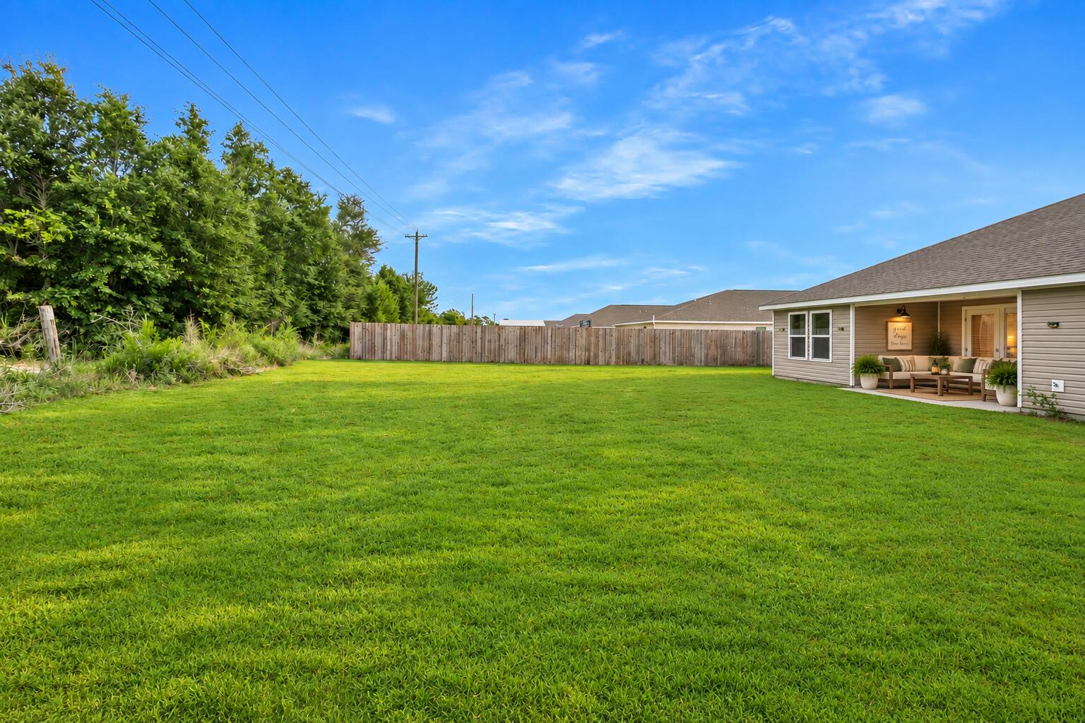 Spacious fenced backyard with a broad green lawn and a covered patio with outdoor seating.