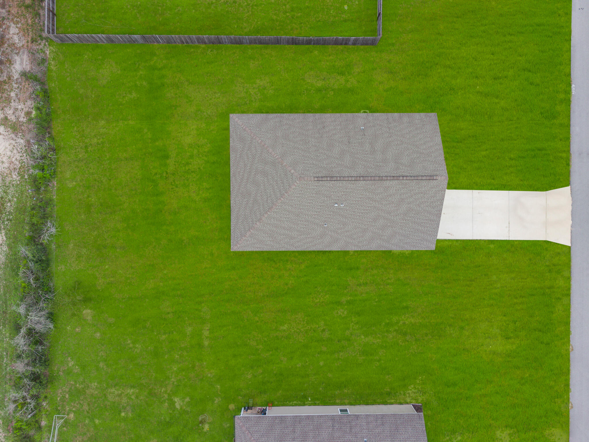Aerial view of a house and broad green lawn beside a concrete driveway.