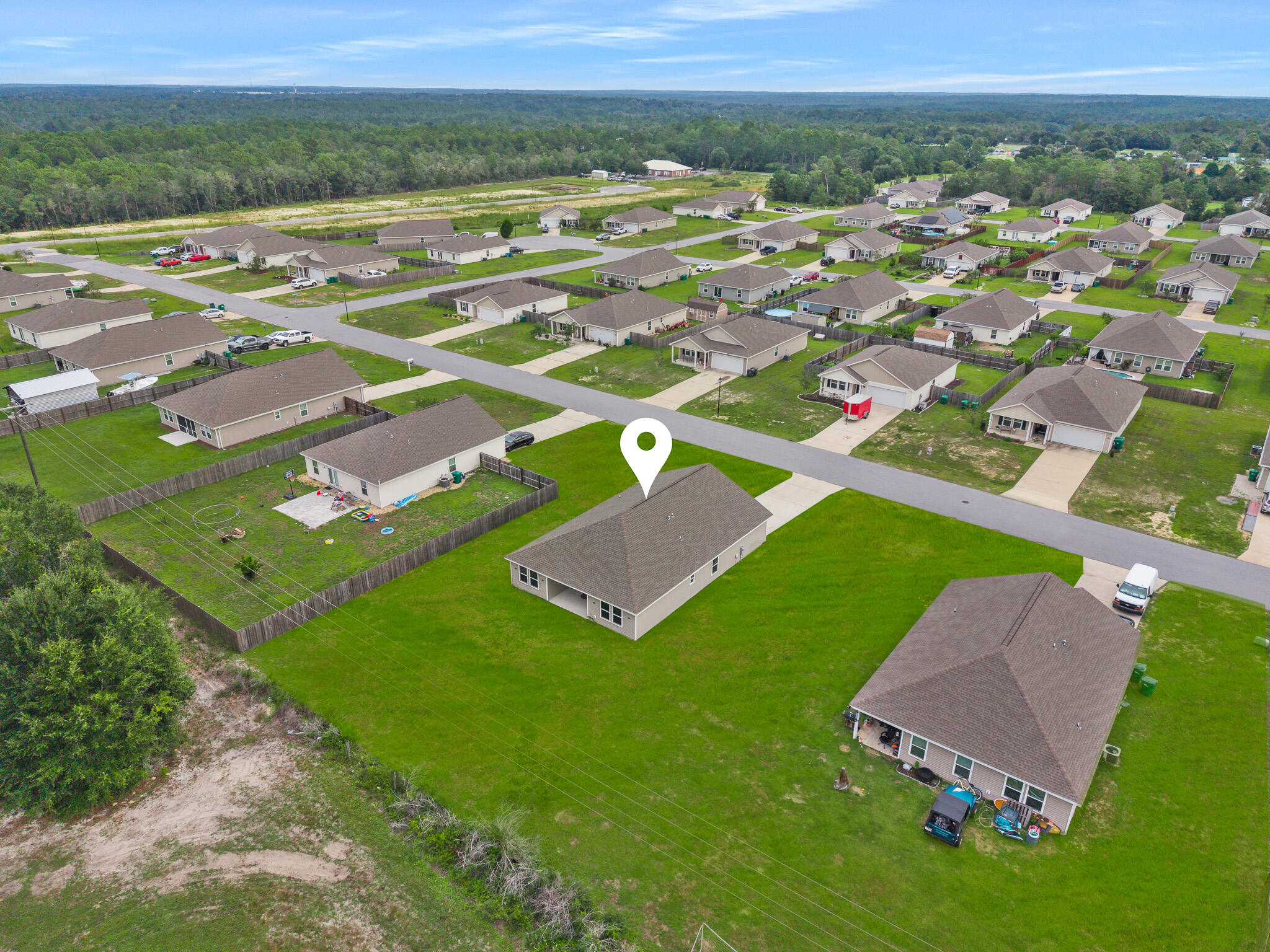 Aerial view of the marked home in a neighborhood of detached houses and broad green lawns.
