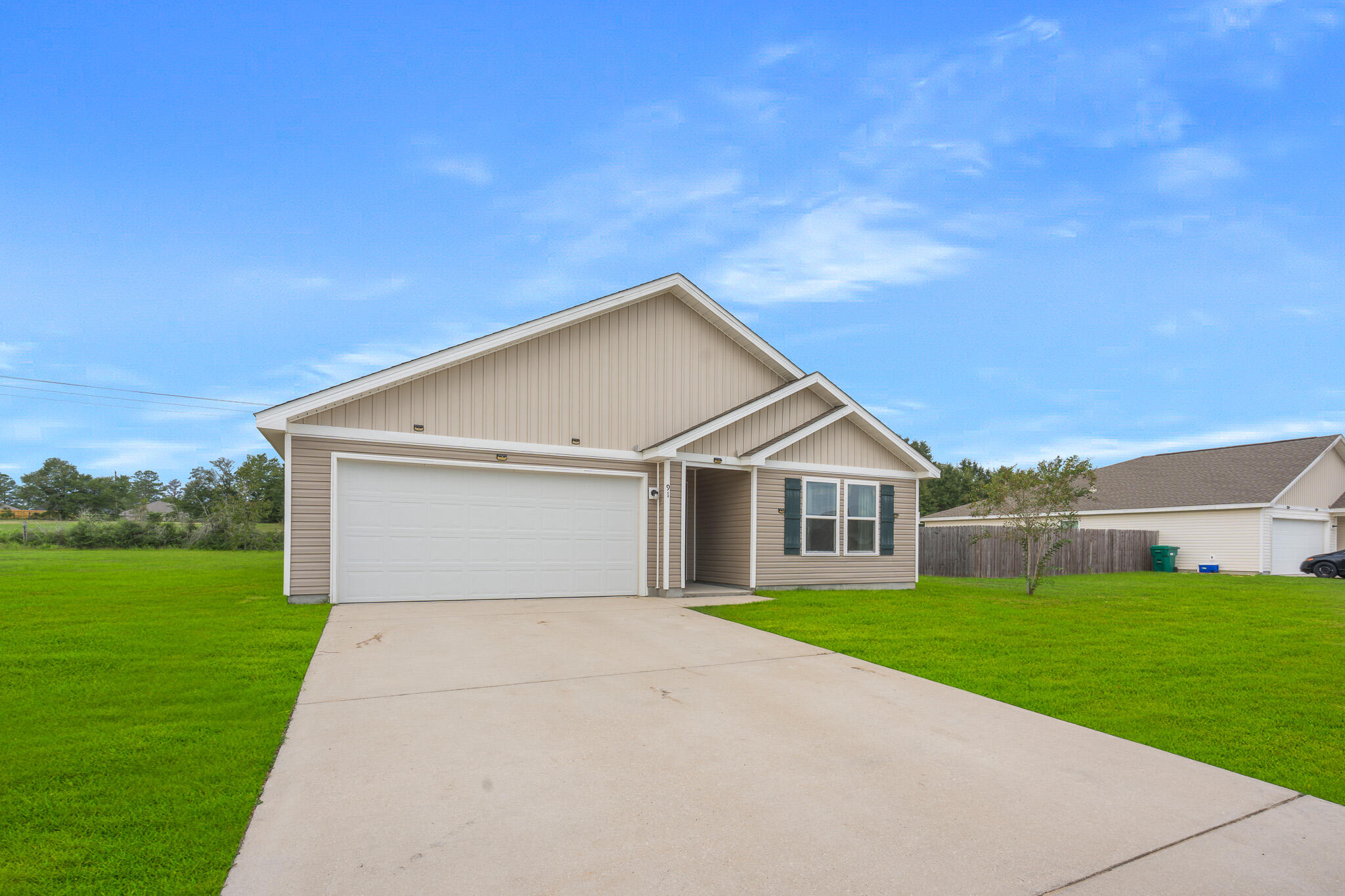 Beige single-story home with a white double garage door, covered entry, and wide concrete driveway.
