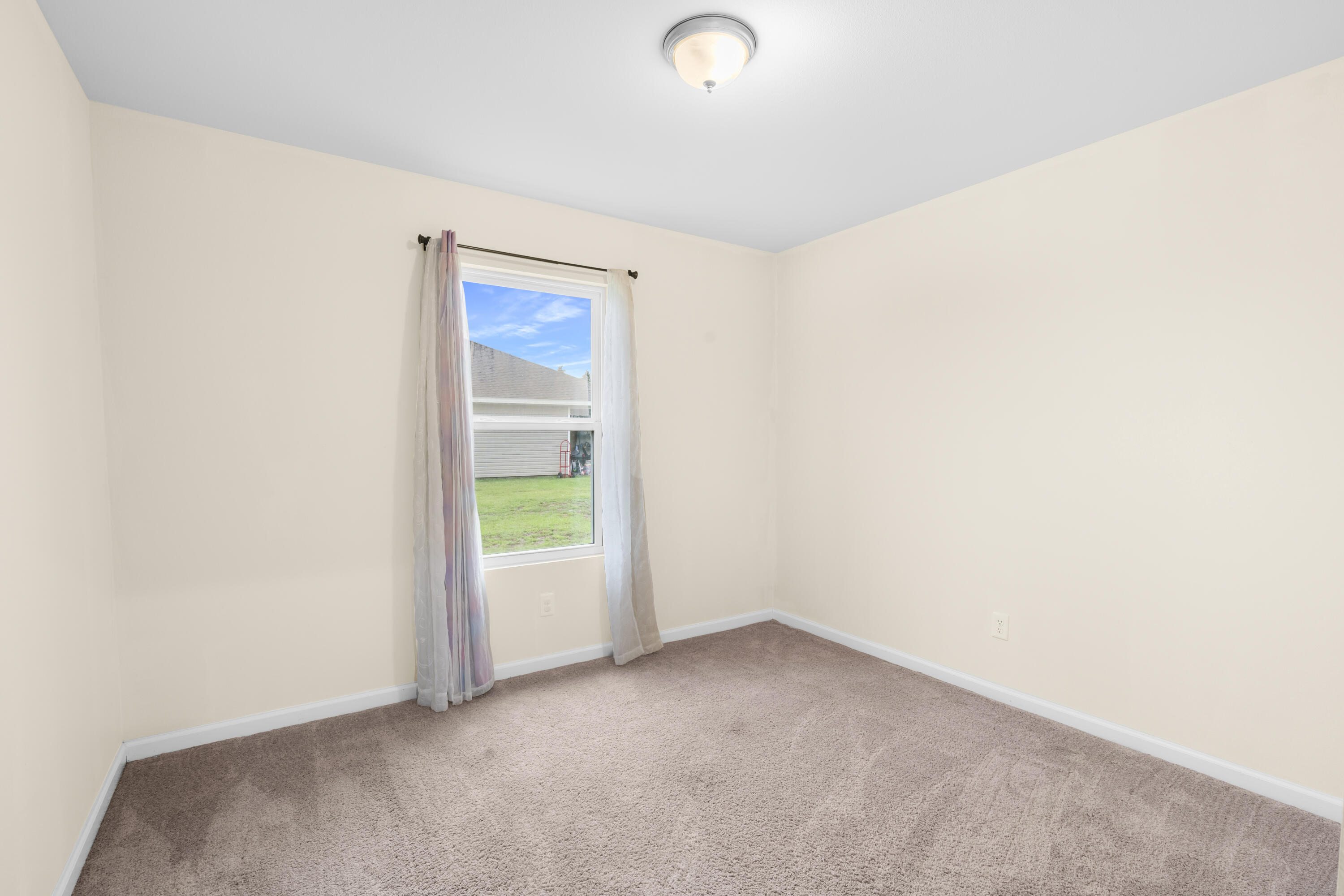 Empty bedroom with beige carpet, pale walls, and a curtained window.