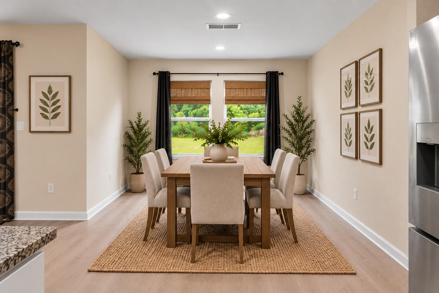 Dining room with a wooden table, upholstered chairs, woven rug, and window overlooking a green lawn.