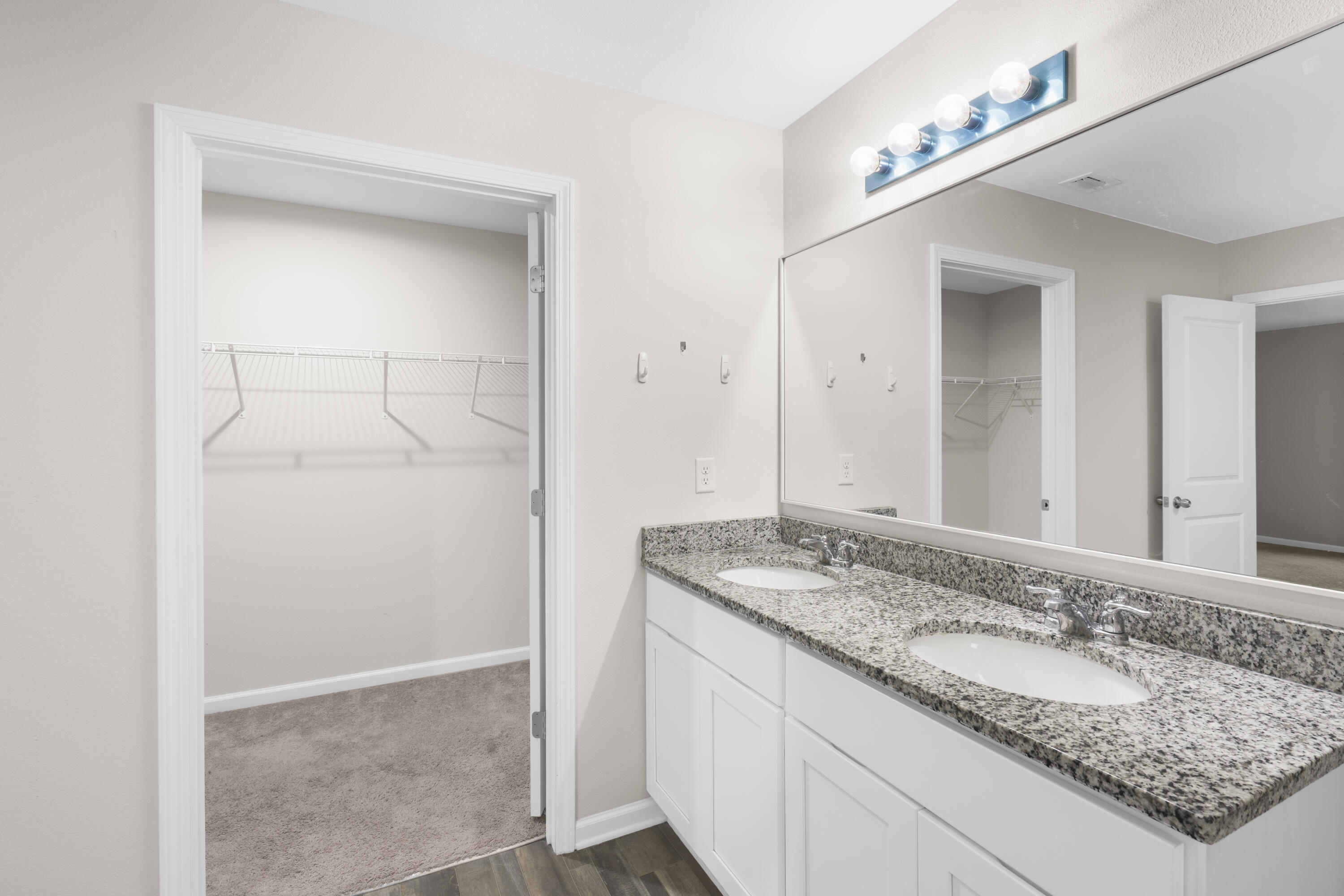 Bathroom with a double-sink granite vanity and an open doorway to a carpeted walk-in closet.