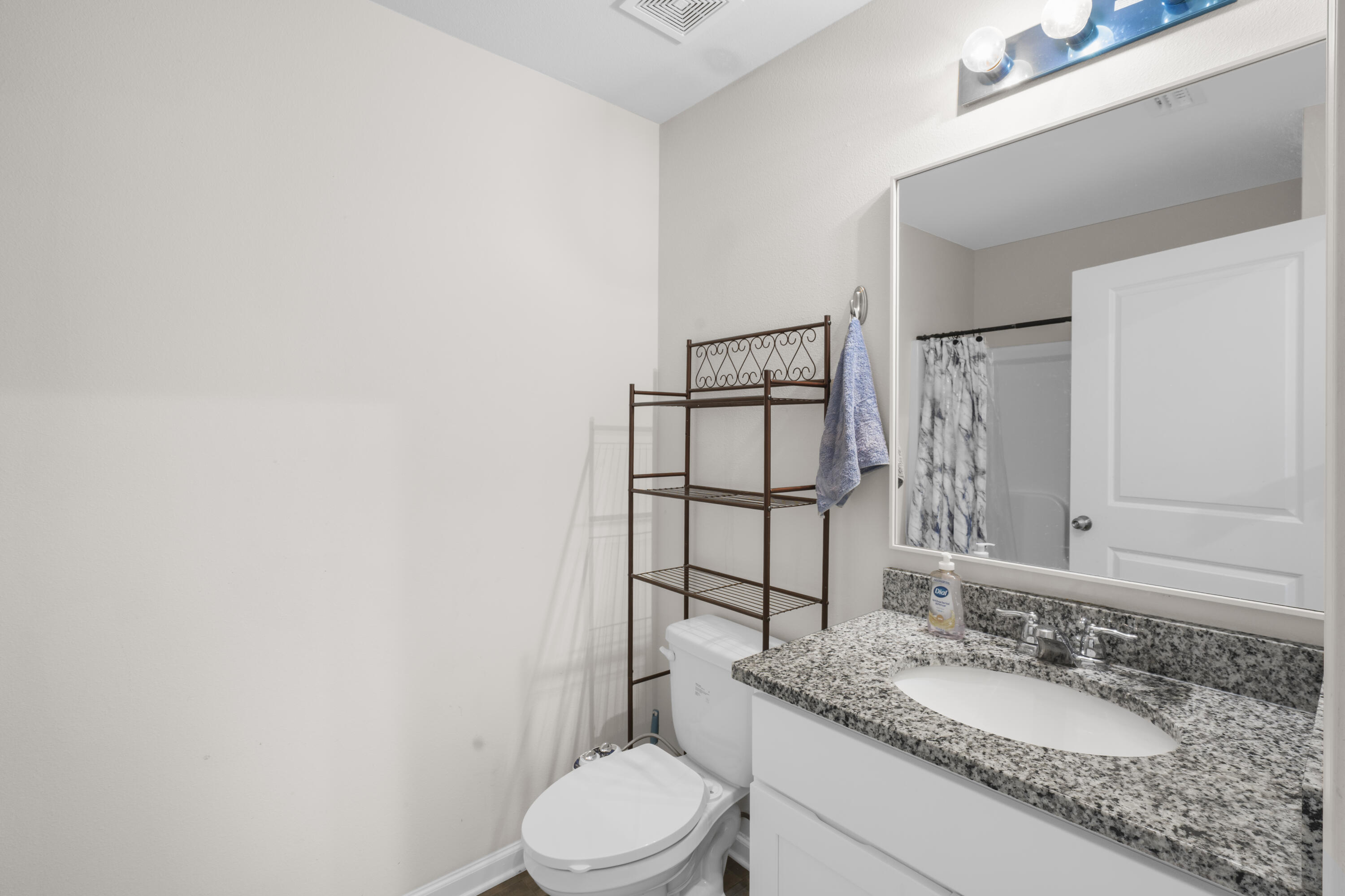 Bathroom with a granite vanity and sink, toilet, large mirror, and patterned shower curtain.