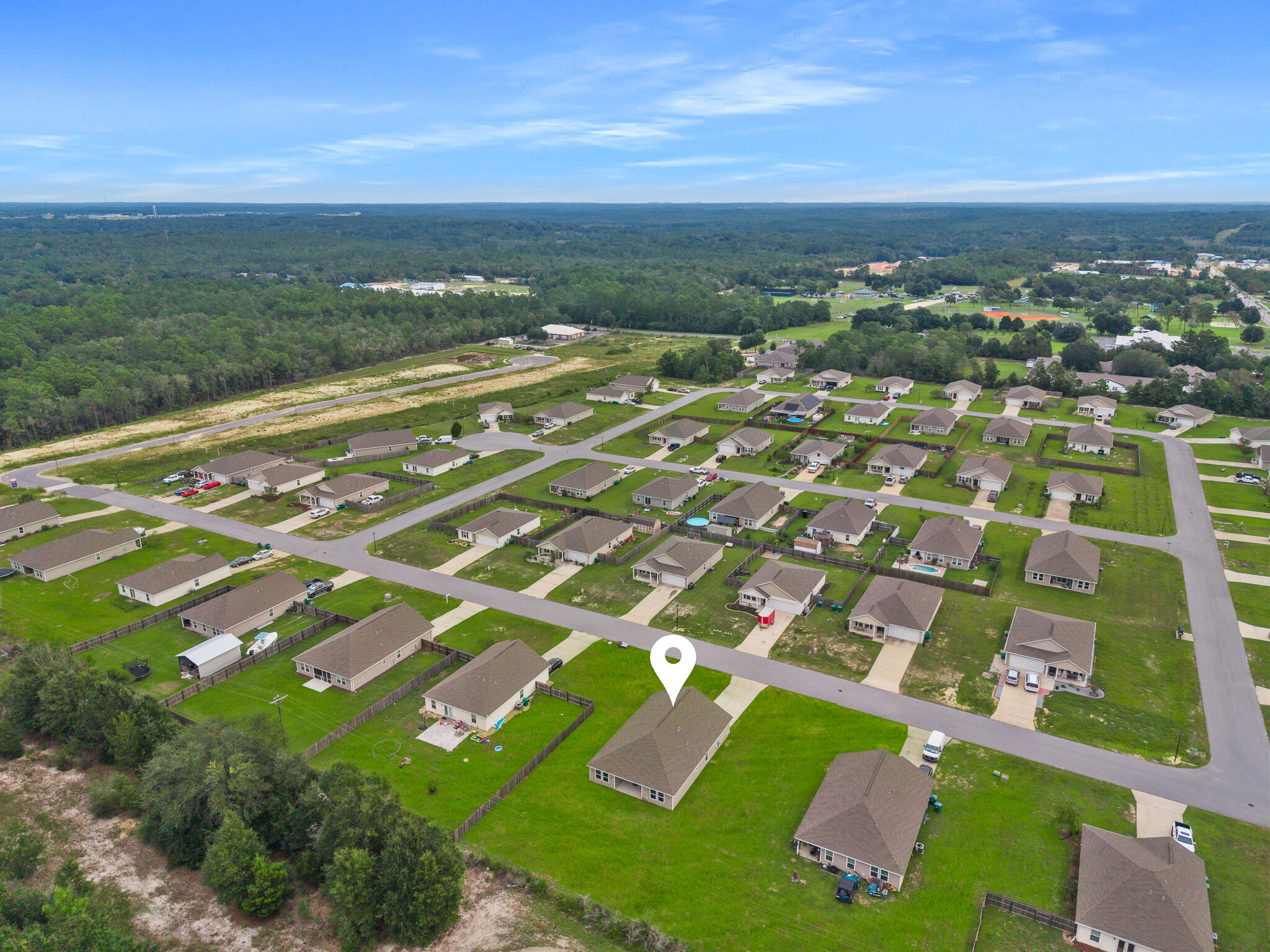 Aerial view of a home marked among neighborhood streets, lawns, and surrounding woodland.