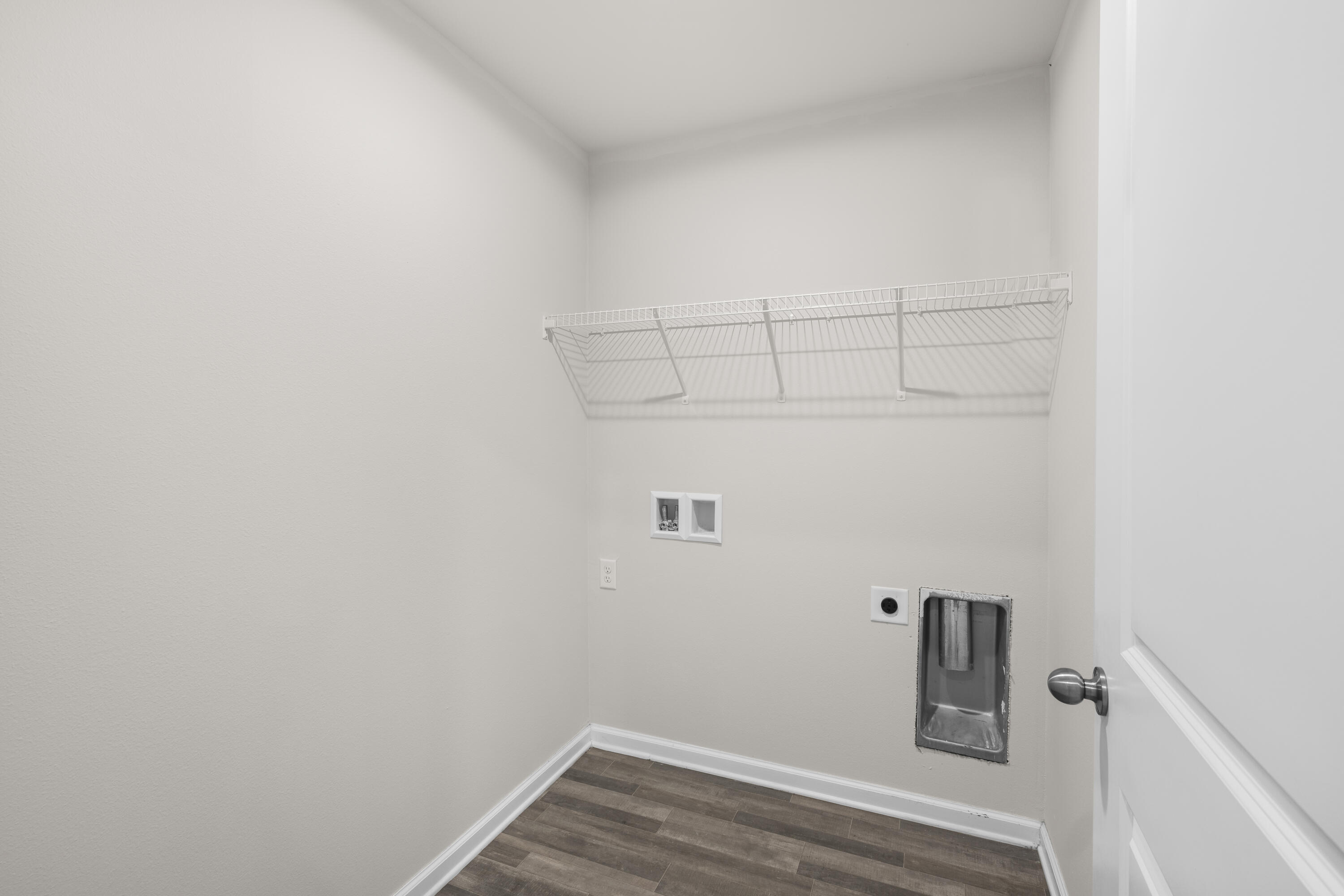 Empty laundry room with wire shelf, washer hookups, and dark tile flooring.