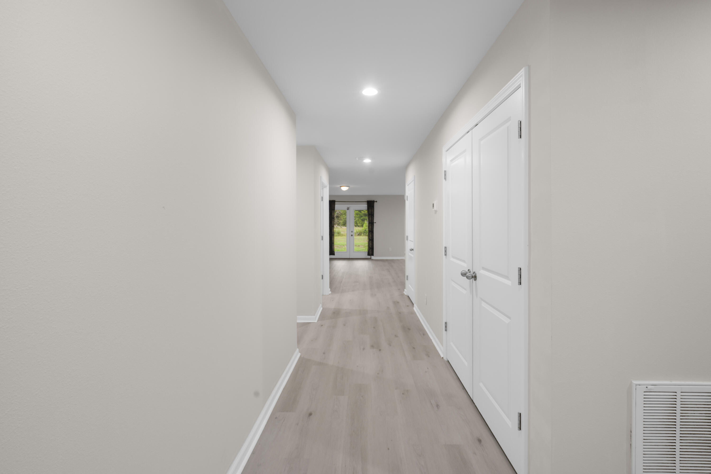Empty hallway with light wood-look floors, white double doors, and glazed doors overlooking greenery.