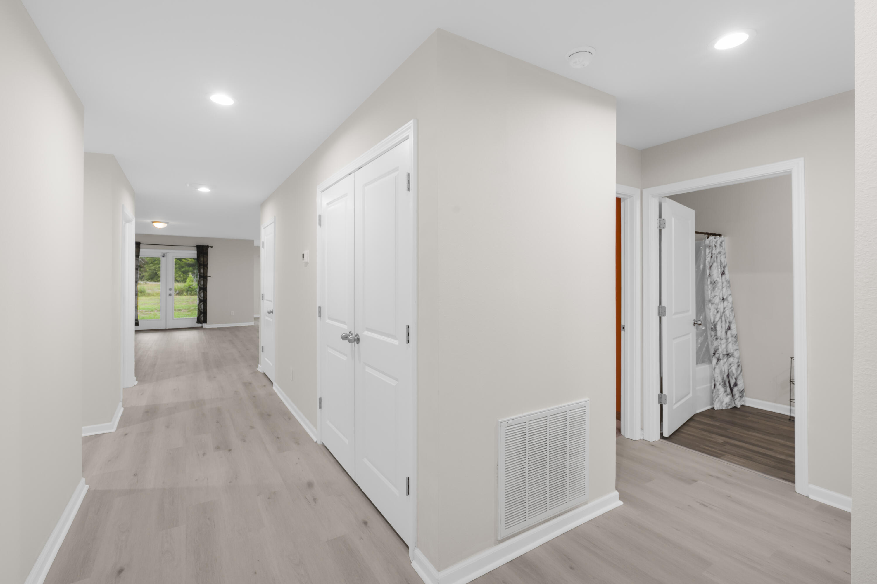 Bright hallway with pale wood-look flooring, white double doors, and glass patio doors at the far end.