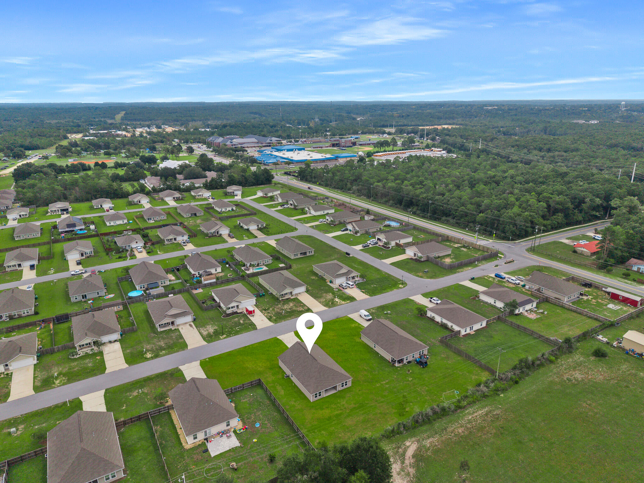 Aerial view of a house marked by a location pin among neighborhood homes and wooded surroundings.