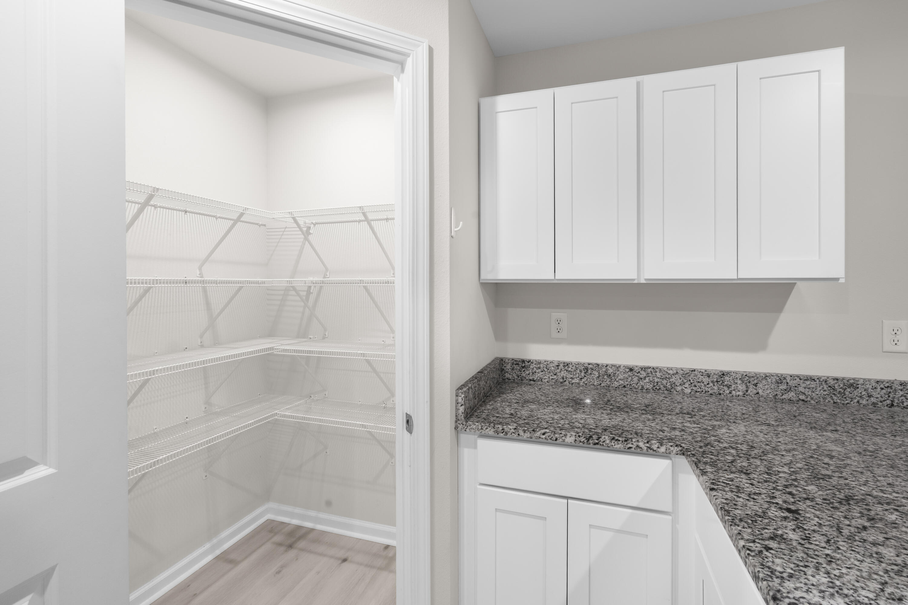 Walk-in pantry with white wire shelves beside white cabinets and a speckled granite countertop.