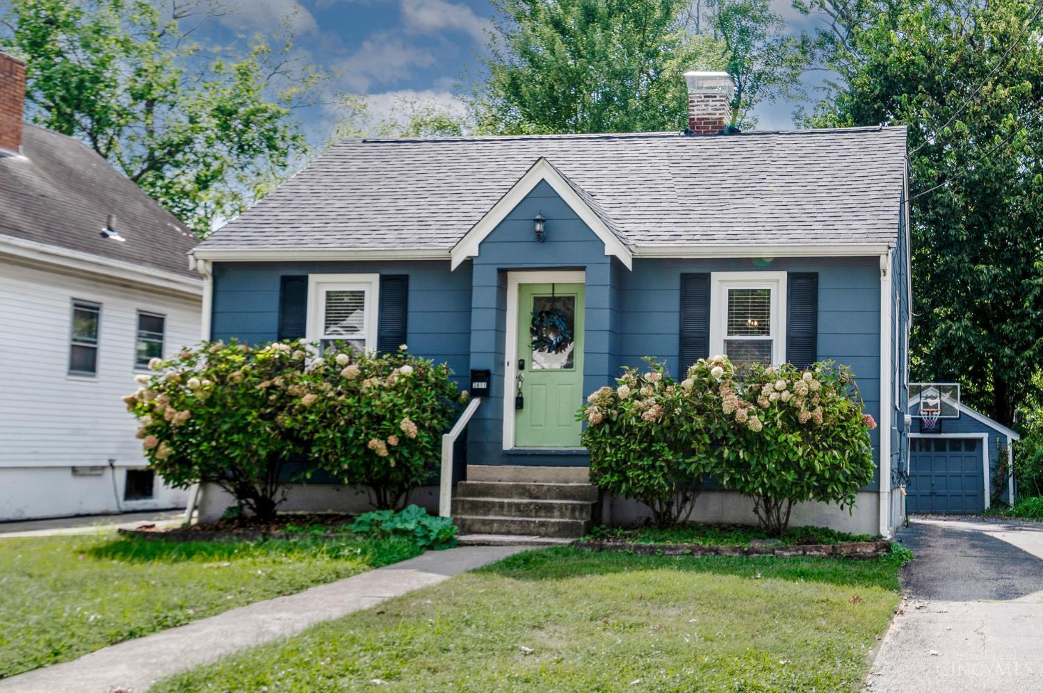 Blue-sided house with a pale green front door, flowering hydrangeas, and a detached garage.