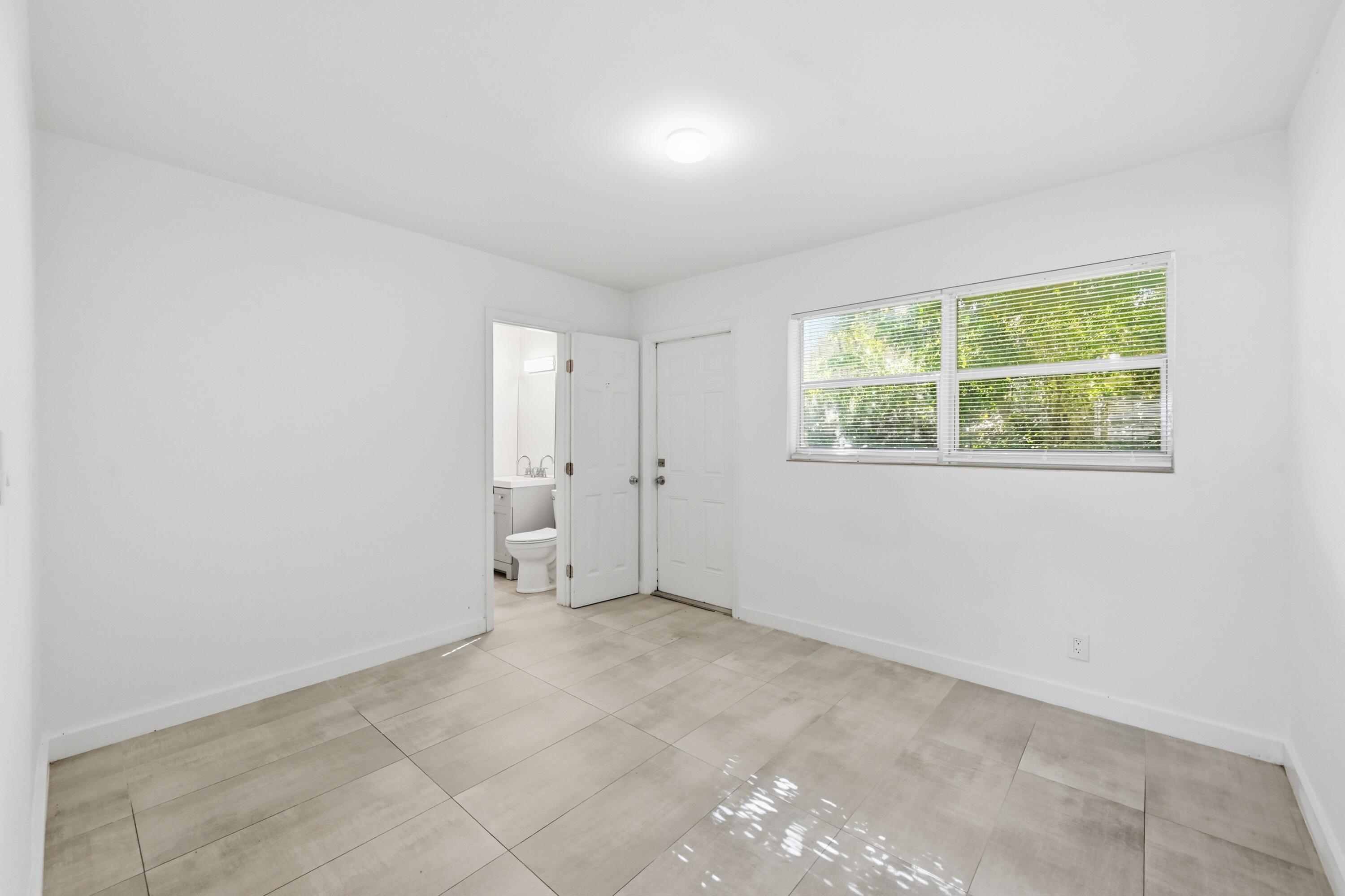 Empty tiled room with a wide window and an open doorway to a bathroom.