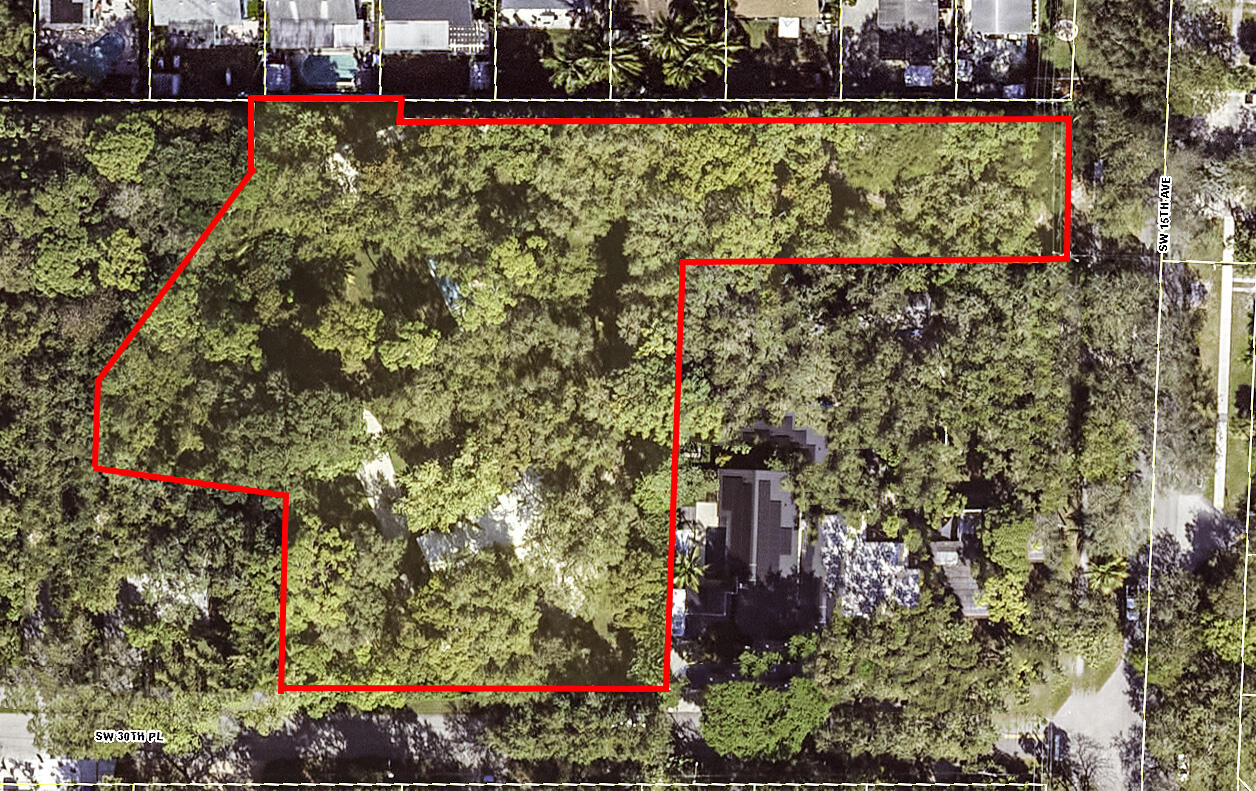 Aerial view of a wooded parcel outlined in red, with homes and streets around it.