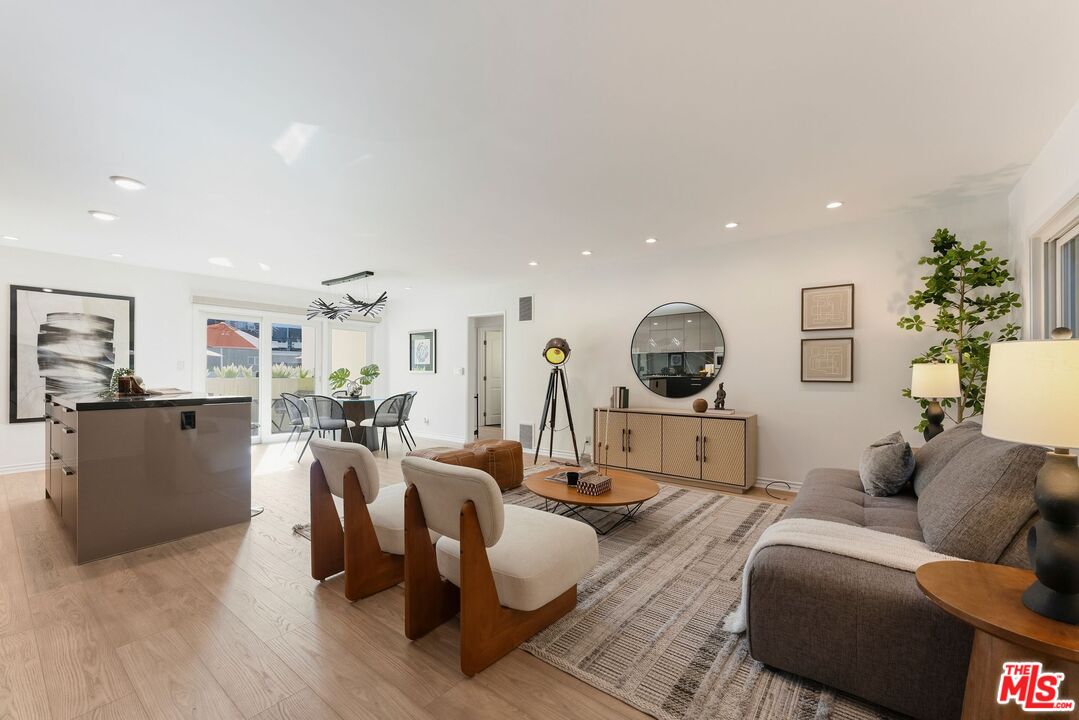 Open-plan living room with a gray sofa, wood-frame chairs, and dining area beside the kitchen.