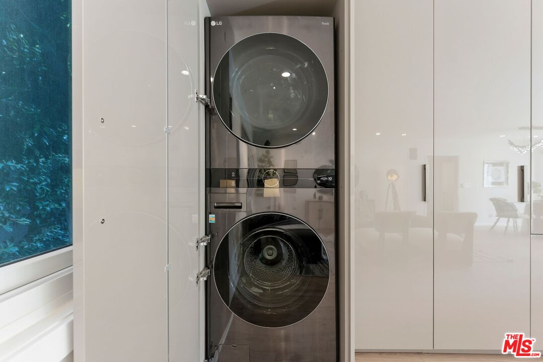 Stacked washer and dryer in a white built-in laundry cabinet beside a window.