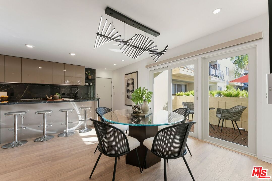 Dining area with a round glass table beside a modern kitchen and sliding doors to a patio.