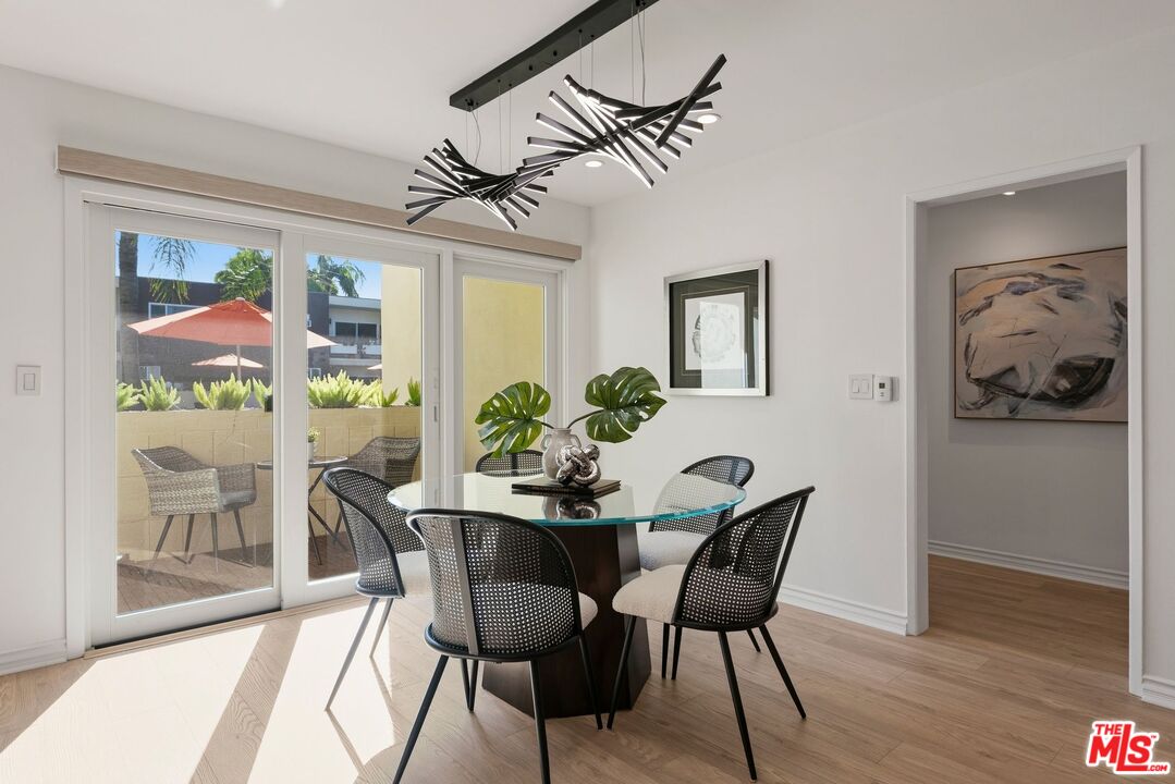 Dining room with a glass table, sculptural chandelier, and sliding doors to a sunny patio.