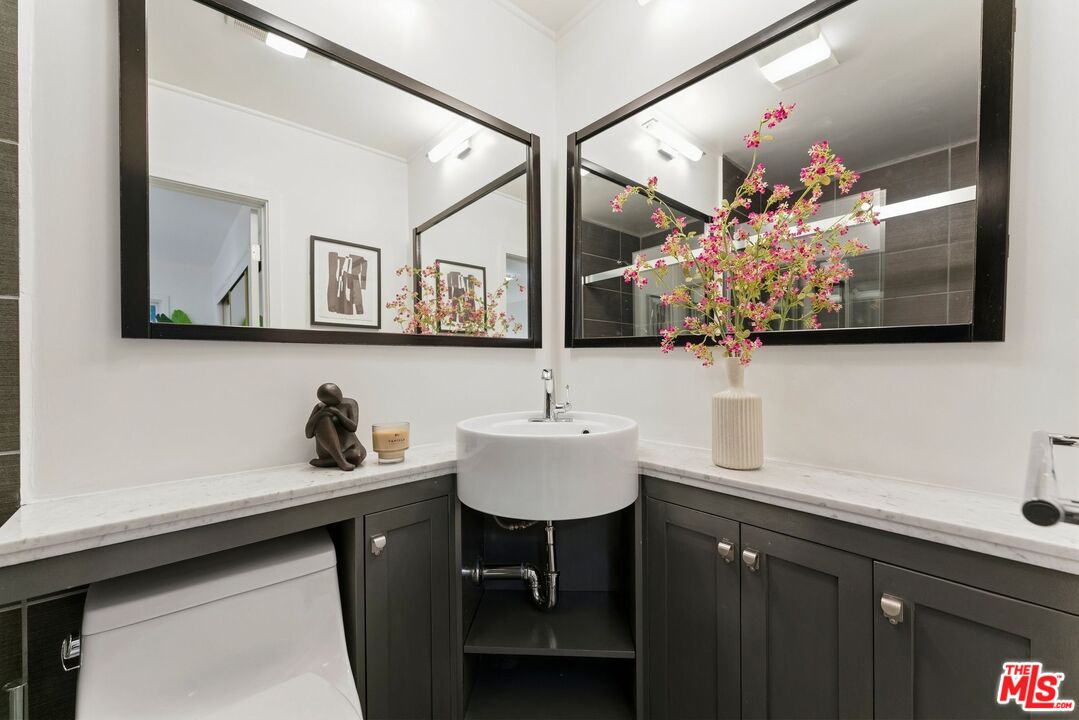 Bathroom vanity with a round vessel sink, marble counter, dark cabinetry, and large mirrors.