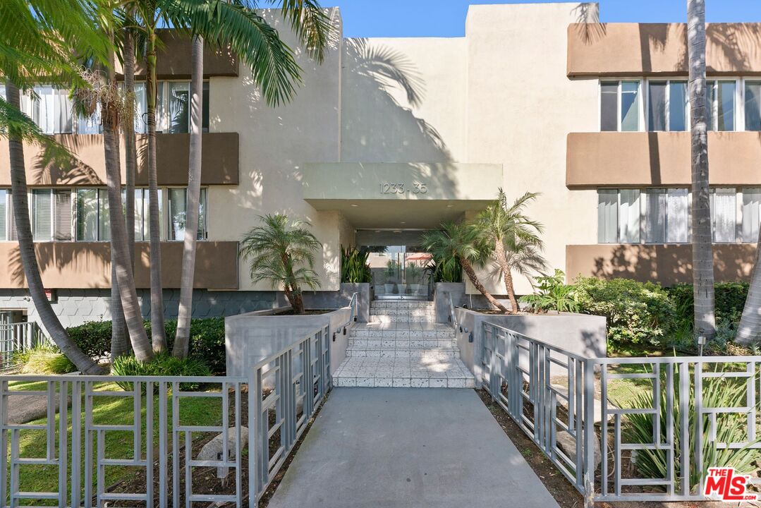 Residential building entrance with tiled steps, metal railings, and palm trees.