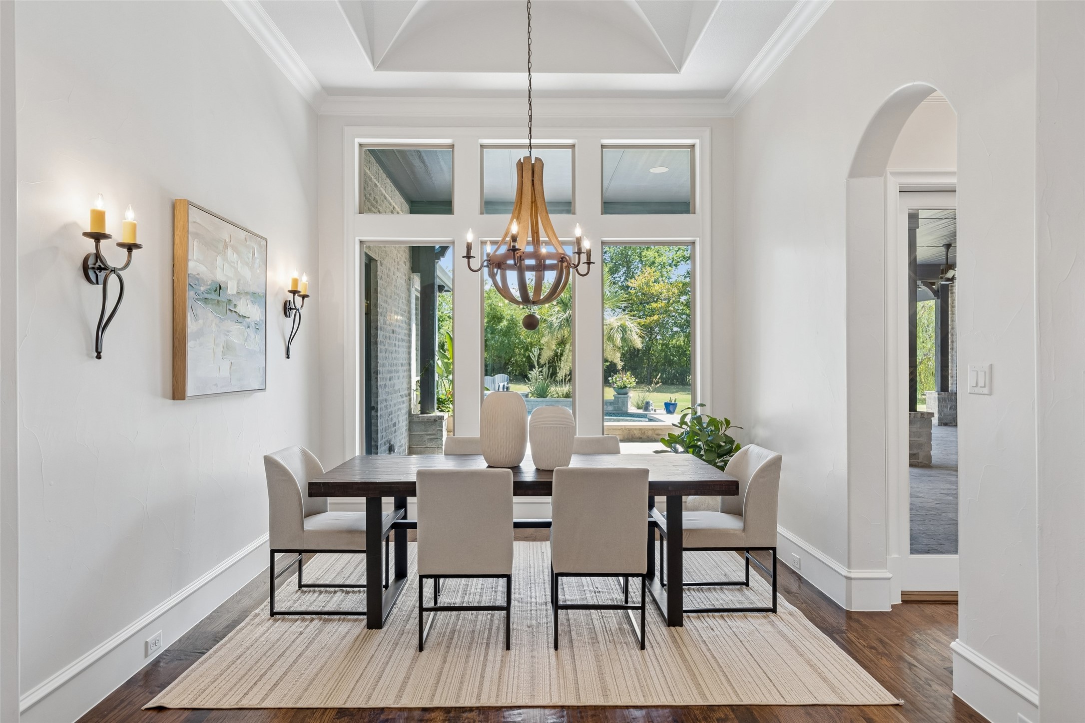 Dining room with a coffered ceiling, chandelier, and tall windows overlooking a swimming pool.
