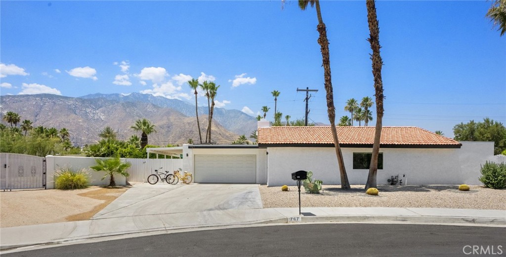 Single-story white Palm Springs home with a tile roof, tall palms, and mountains behind it.