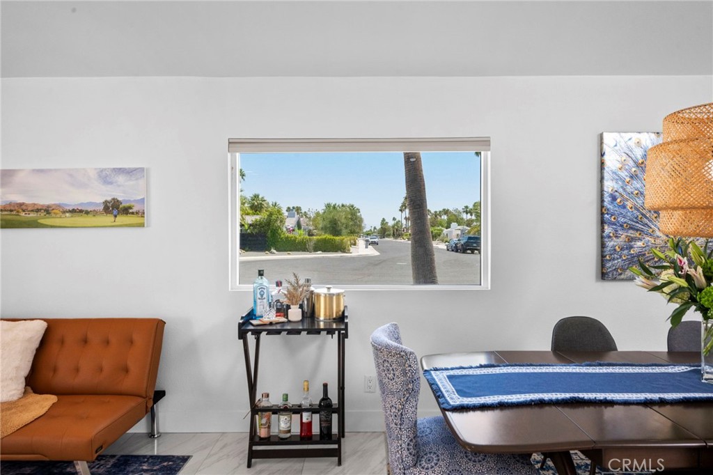 Dining area with a blue table runner and orange leather sofa beside a window overlooking a palm-lined street.