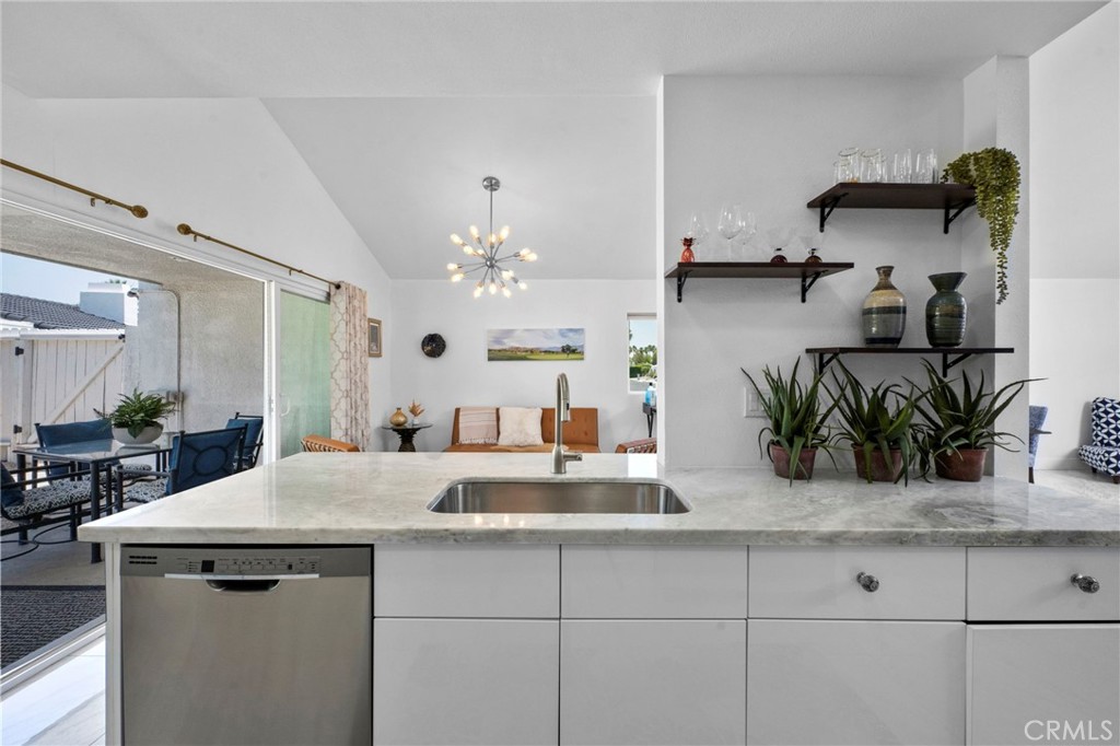 Open-plan kitchen with a stone island, stainless dishwasher, floating shelves, and sliding doors to a patio.