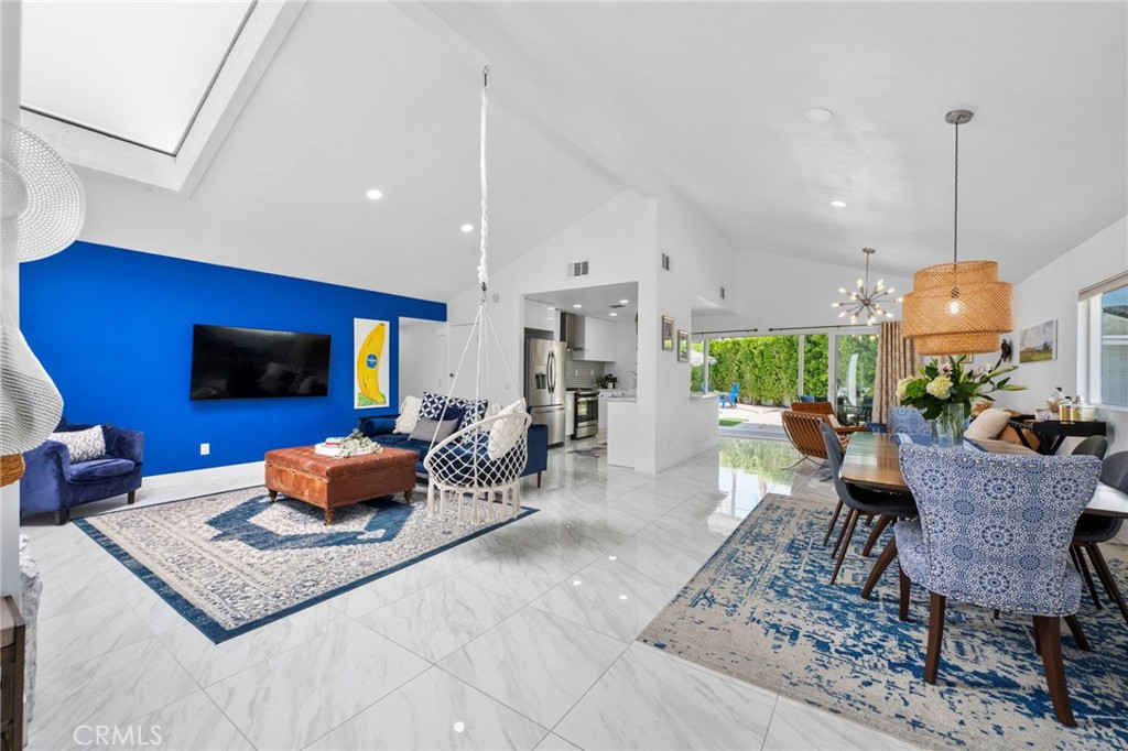 Open-plan living and dining room with a blue accent wall, hanging chair, and marble-look tile floors.