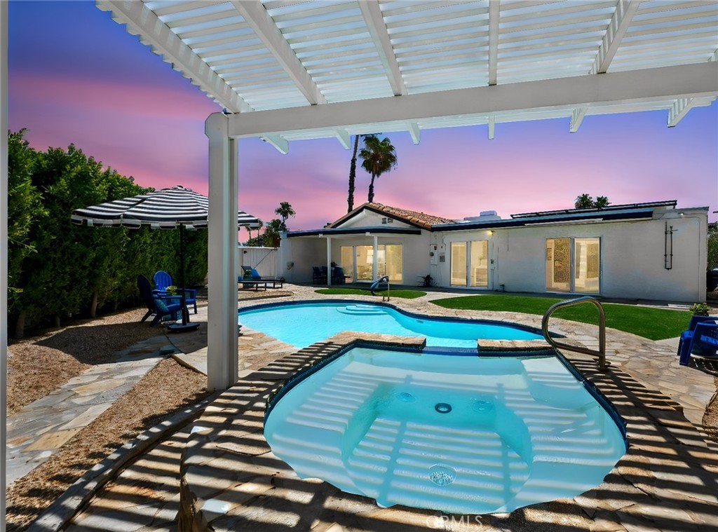 Backyard pool and raised spa beneath a pergola at dusk, with a single-story home beyond.