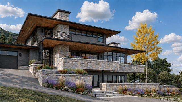 Modern stone-and-timber mountain home with balconies, landscaped terraces, and a yellow autumn tree.