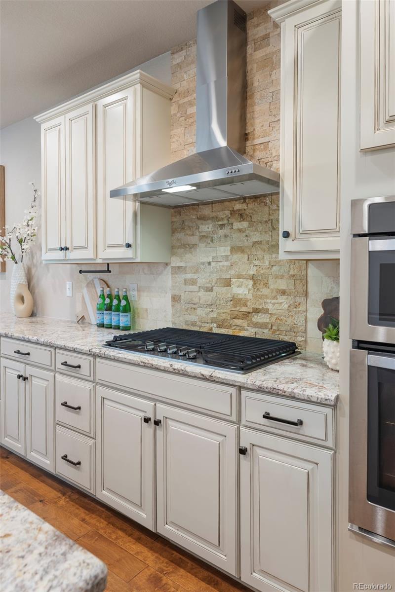 Kitchen with white cabinetry, stone backsplash, granite counters, and a large gas cooktop.