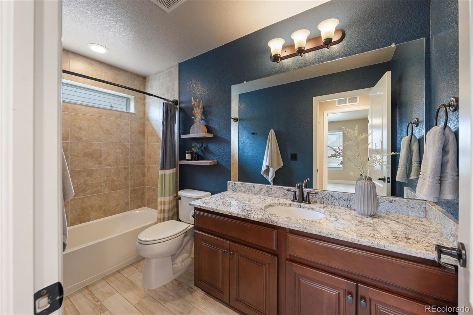 Bathroom with a tan tiled tub surround, blue walls, and a long granite-topped wood vanity.