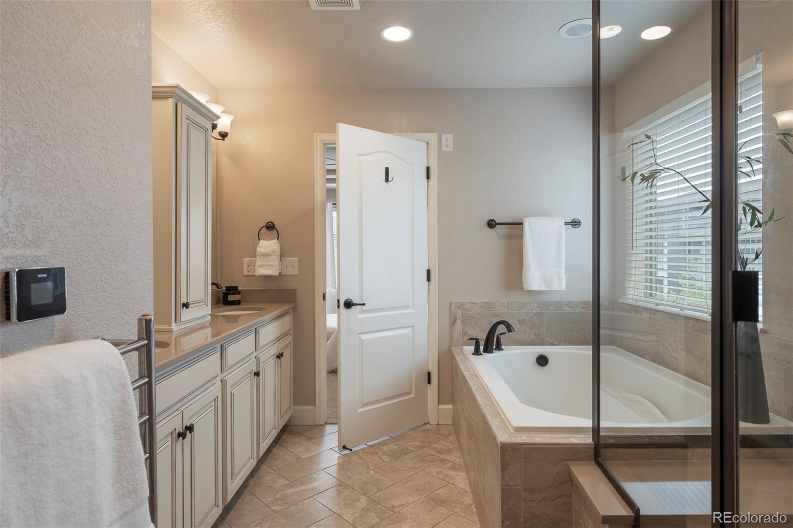 Bathroom with a built-in soaking tub, glass shower enclosure, and long cream vanity.