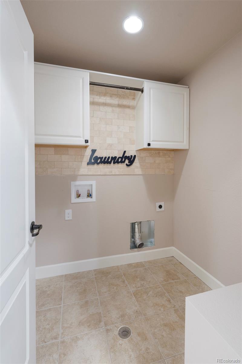 Laundry room with white cabinets, tiled backsplash and floor, and washer hookups.