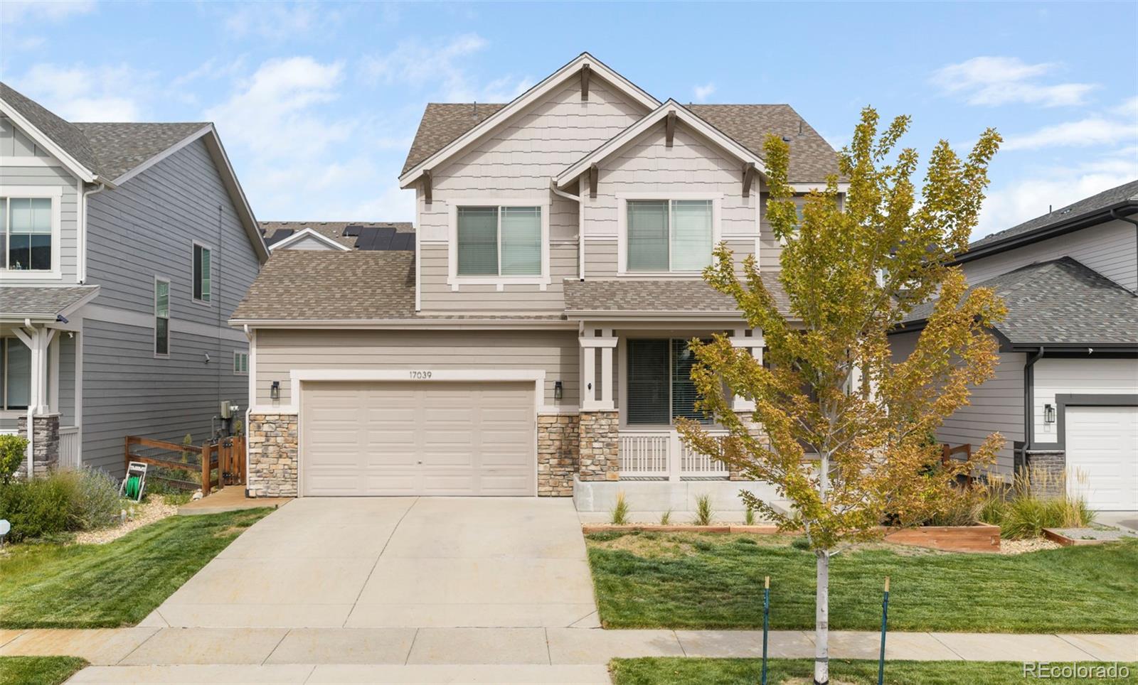 Two-story beige house with a stone-accented facade, two-car garage, and covered porch.