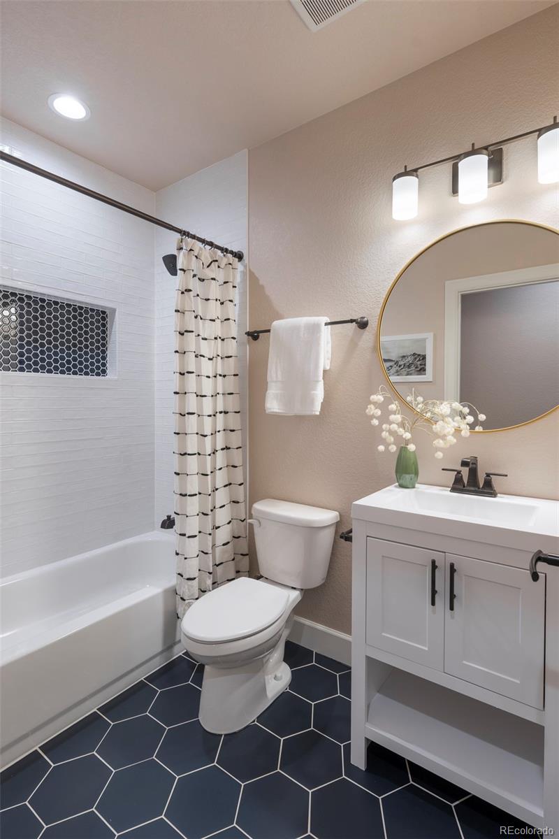 Bathroom with a white tub, black hexagonal tile niche, white vanity, and dark geometric floor tiles.