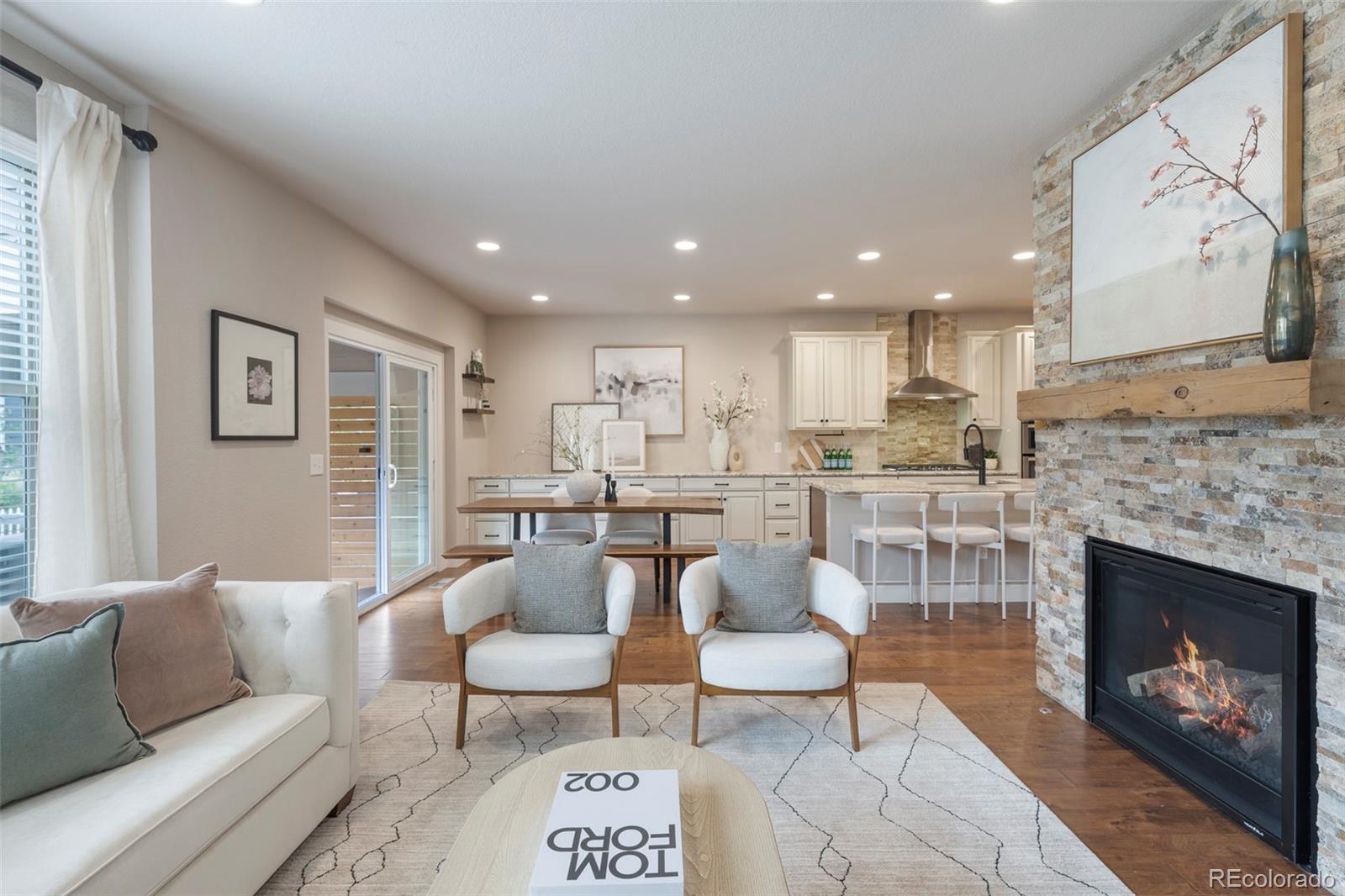 Open-plan living room with a stone fireplace, white seating, and the kitchen and dining area beyond.
