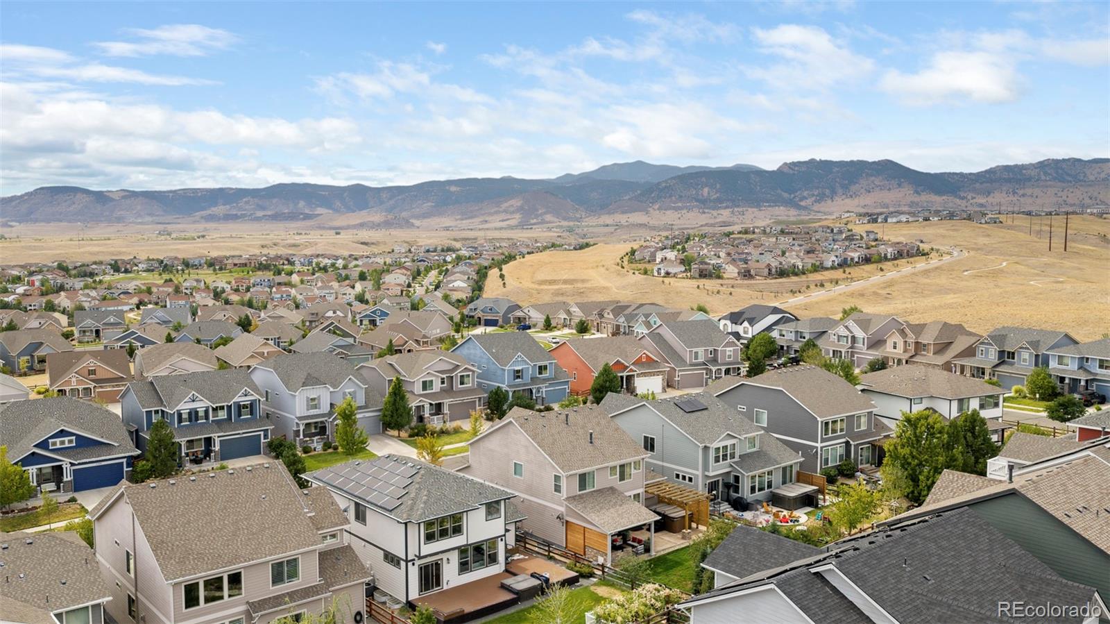 Aerial view of a suburban neighborhood with open grassland and mountains beyond.