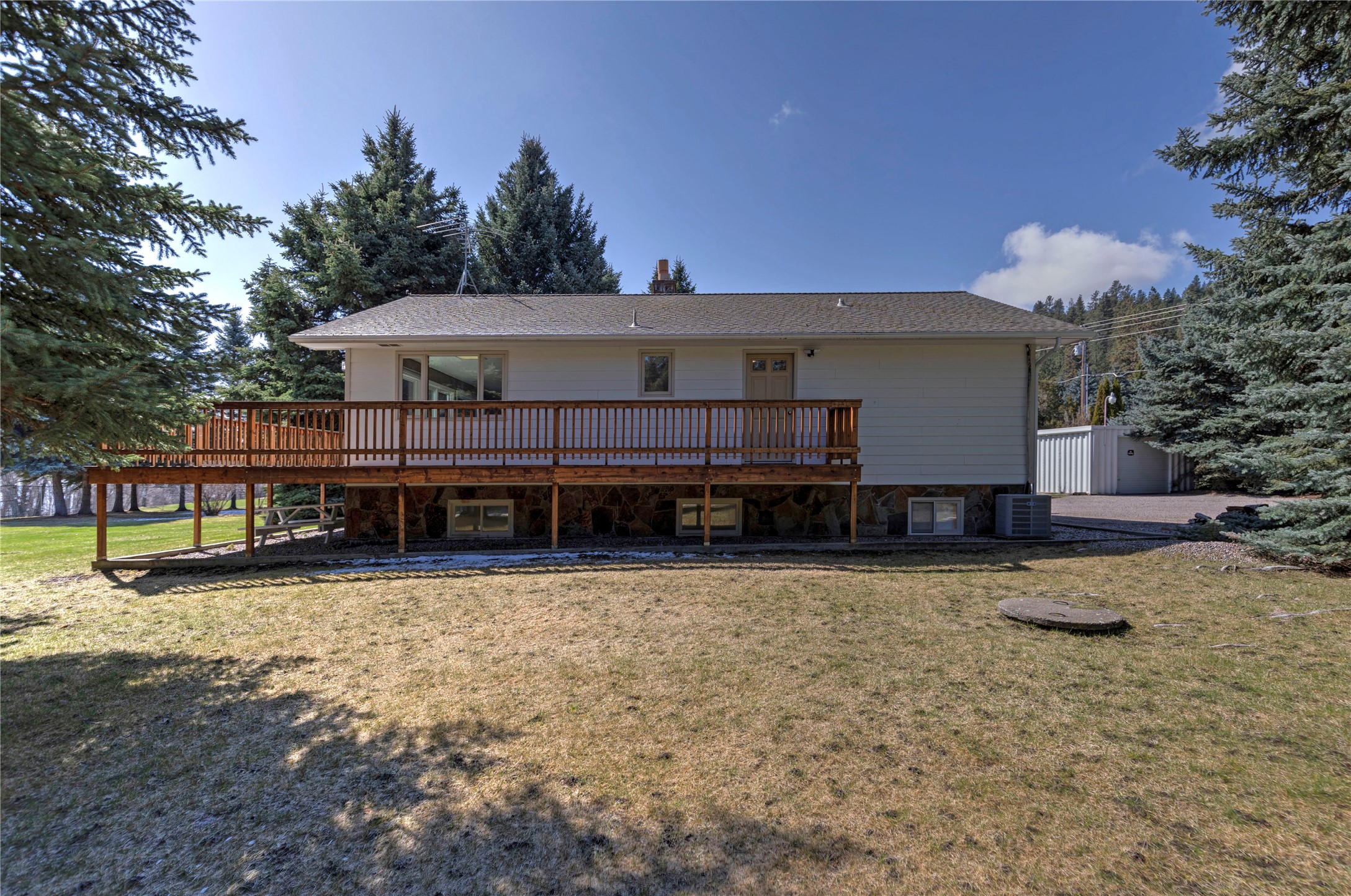House exterior with a long raised wooden deck, stone foundation, and evergreen trees.