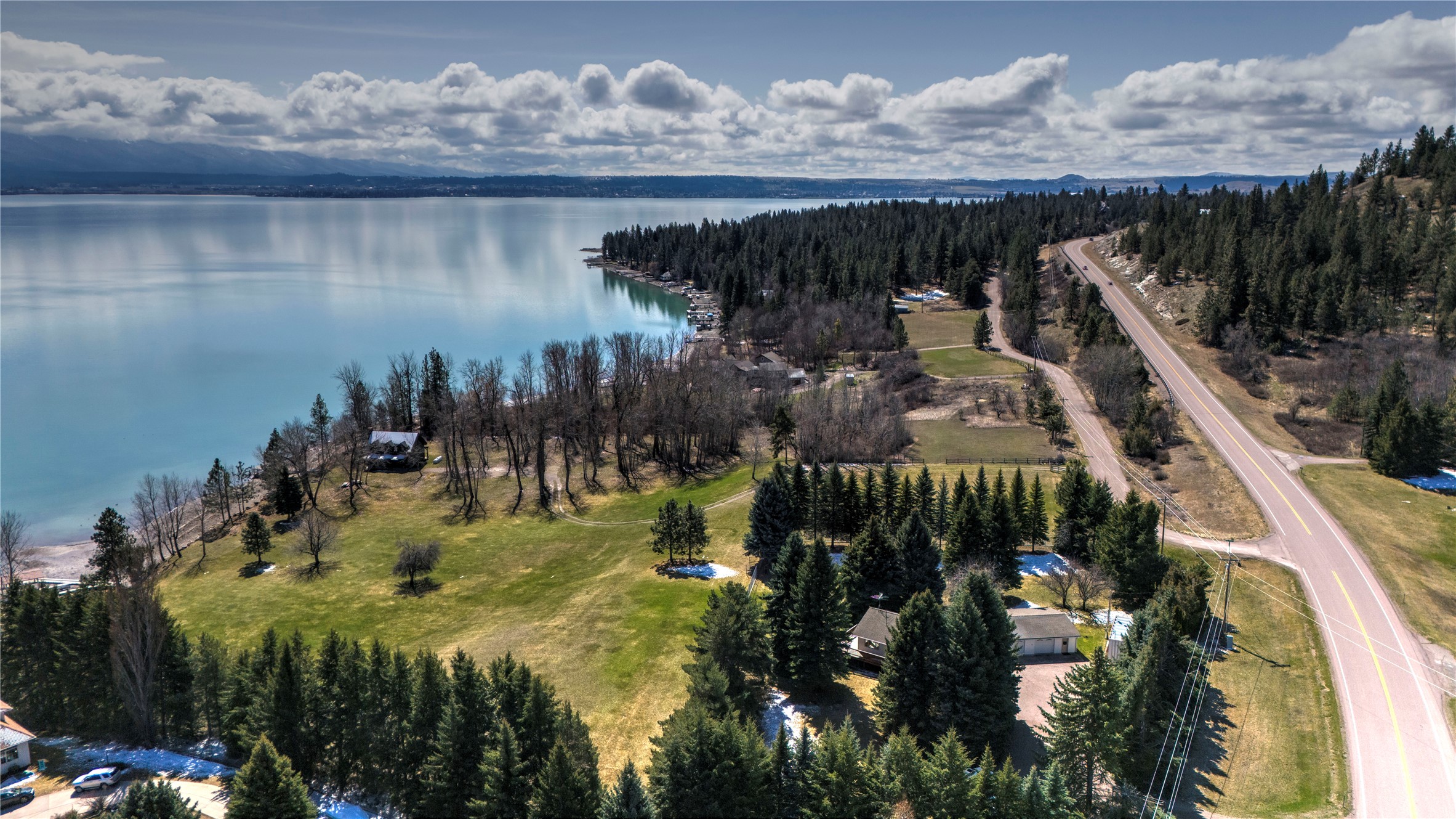 Aerial view of a wooded lakeside property with open lawn, homes, and a road along the shore.