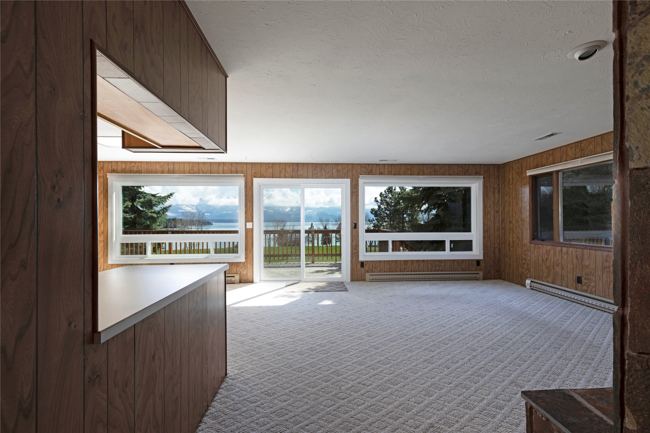 Vacant wood-paneled living room with lake and mountain views through wide windows and sliding glass doors.