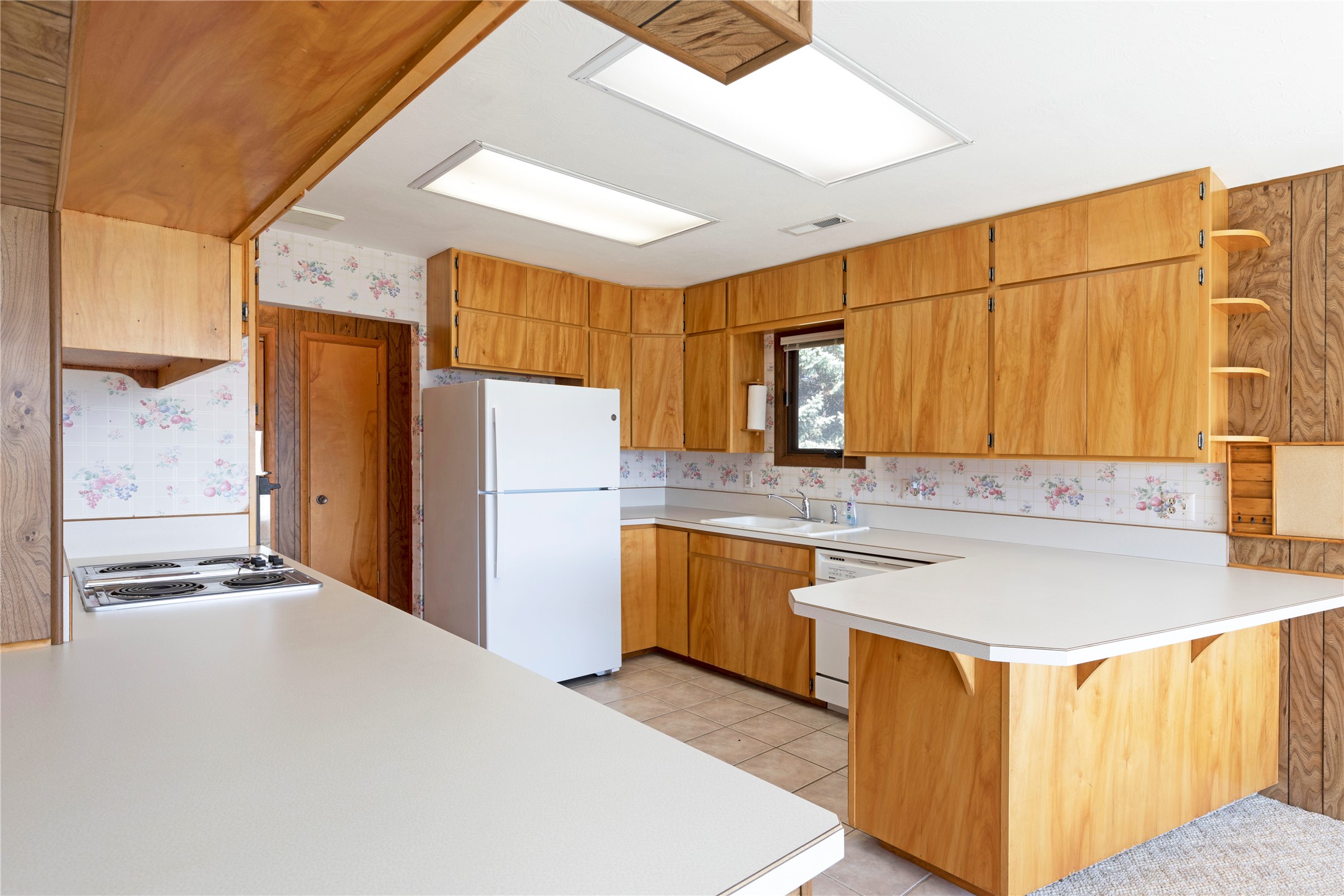Kitchen with honey-colored wood cabinets, a large white peninsula, and floral tile backsplash.