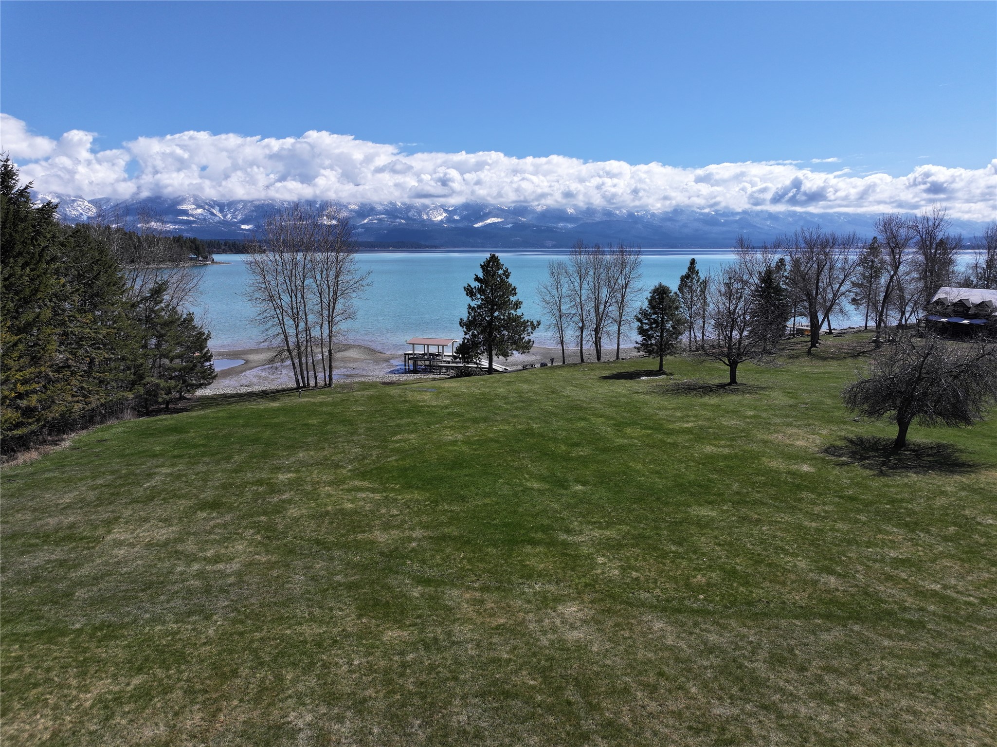Lakeside lawn and dock overlook blue water and snow-dusted mountains.