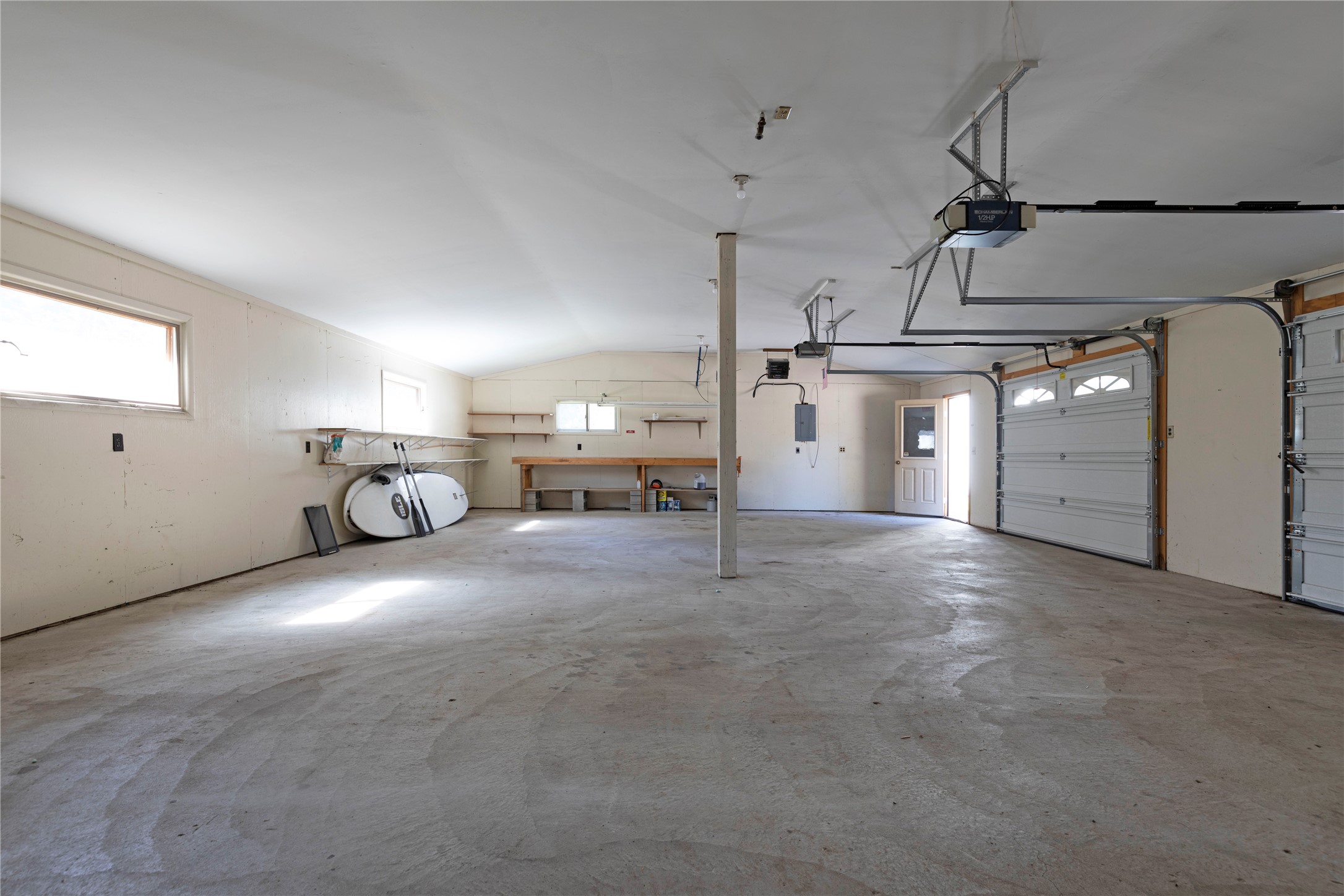Spacious garage with two overhead doors, concrete floor, wall shelving, and a kayak.