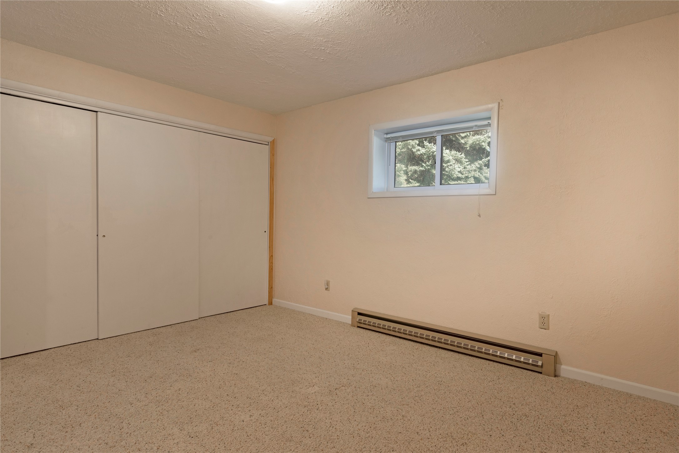 Empty bedroom with sliding closet doors, beige carpet, and a small window.