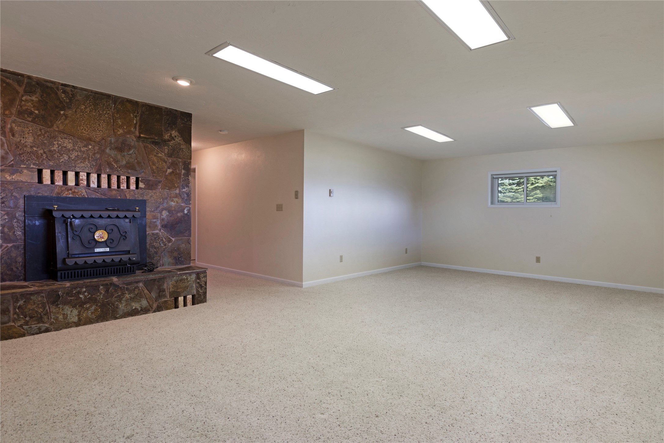 Empty carpeted room with a stone fireplace and small window.